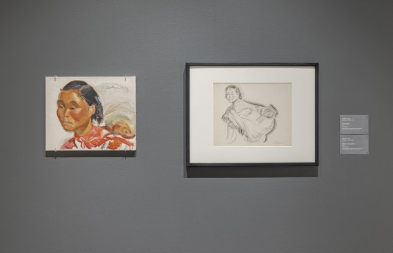 Grey wall with two artworks hung on them. A portrait of a woman of color on the left, with a conte sketch hung to the right of it.