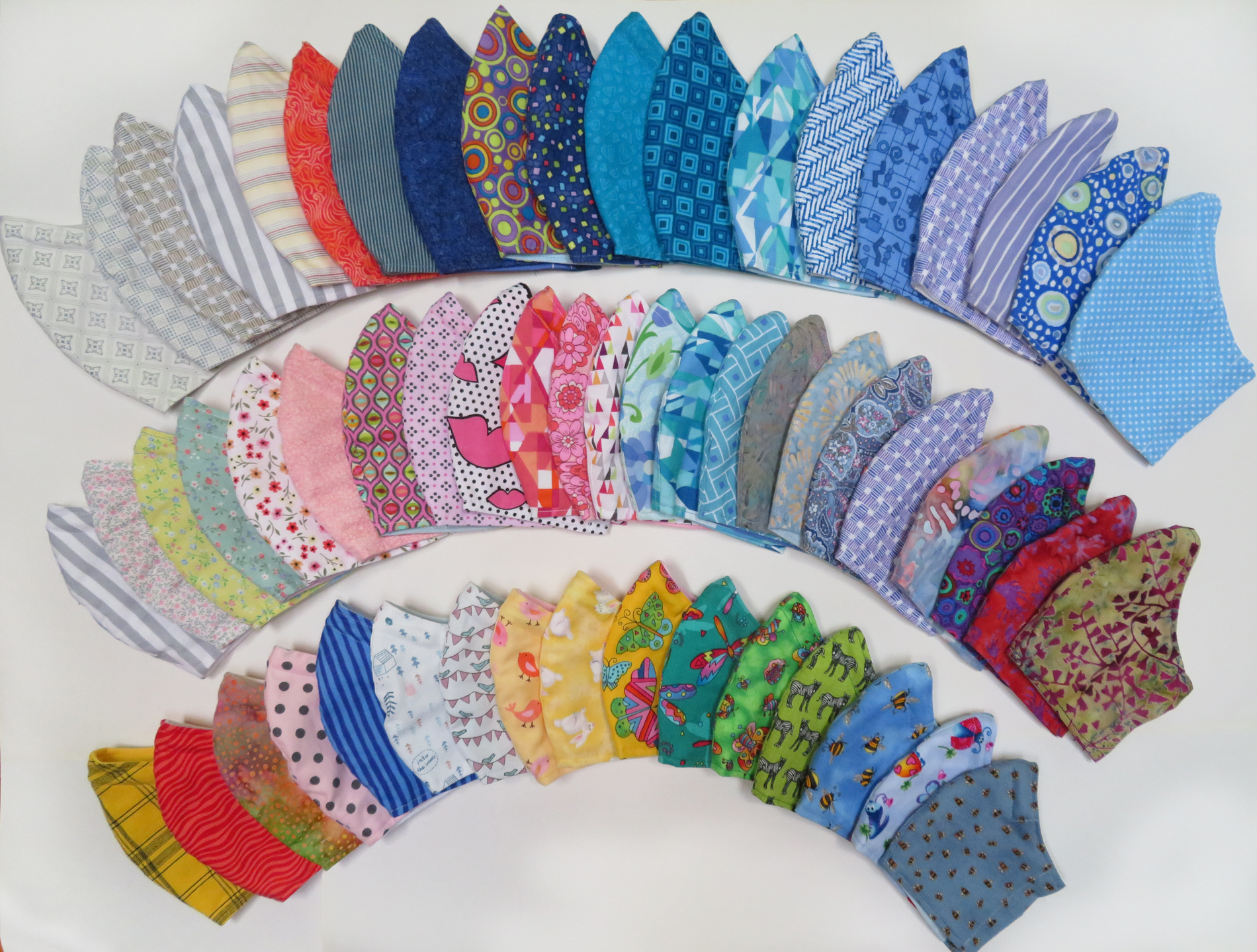 Face masks laid flat in three arcing rows to show range of colours and patterns