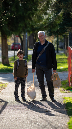 Vertical still image of an older man and his young son on a sidewalk holding a canvas shopping bag between them