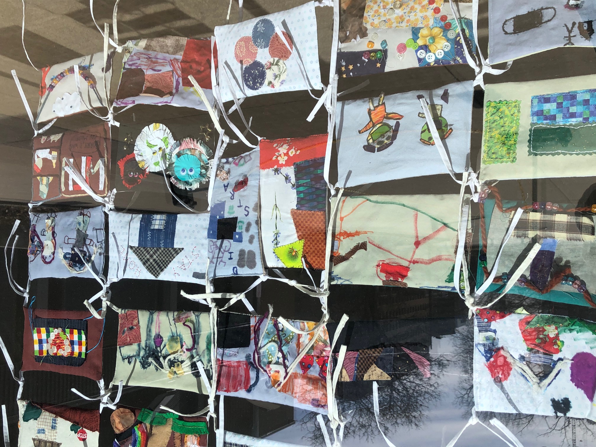 View of community quilt made of face masks tied together and hanging behind a window
