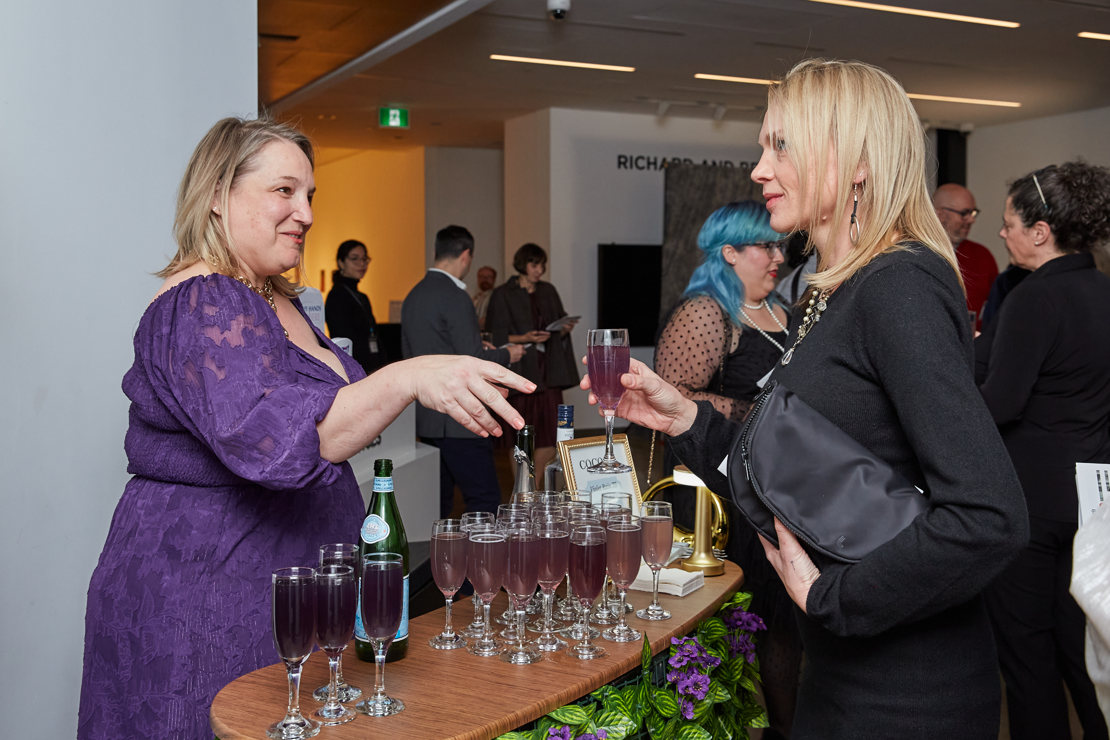 Image of a women reaching her hand out to receive a glass of wine being served to her