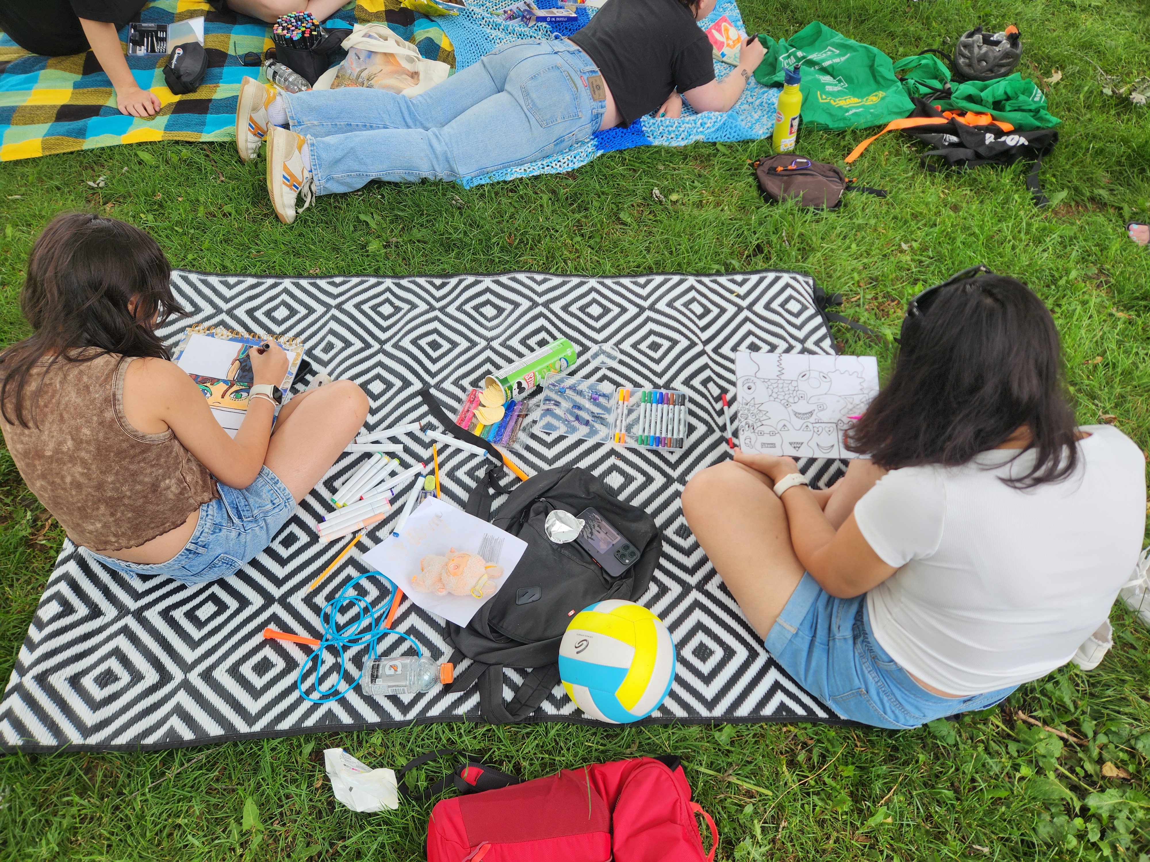 Photo from above of two young persons sitting cross-legged on a blanket with art supplies around them