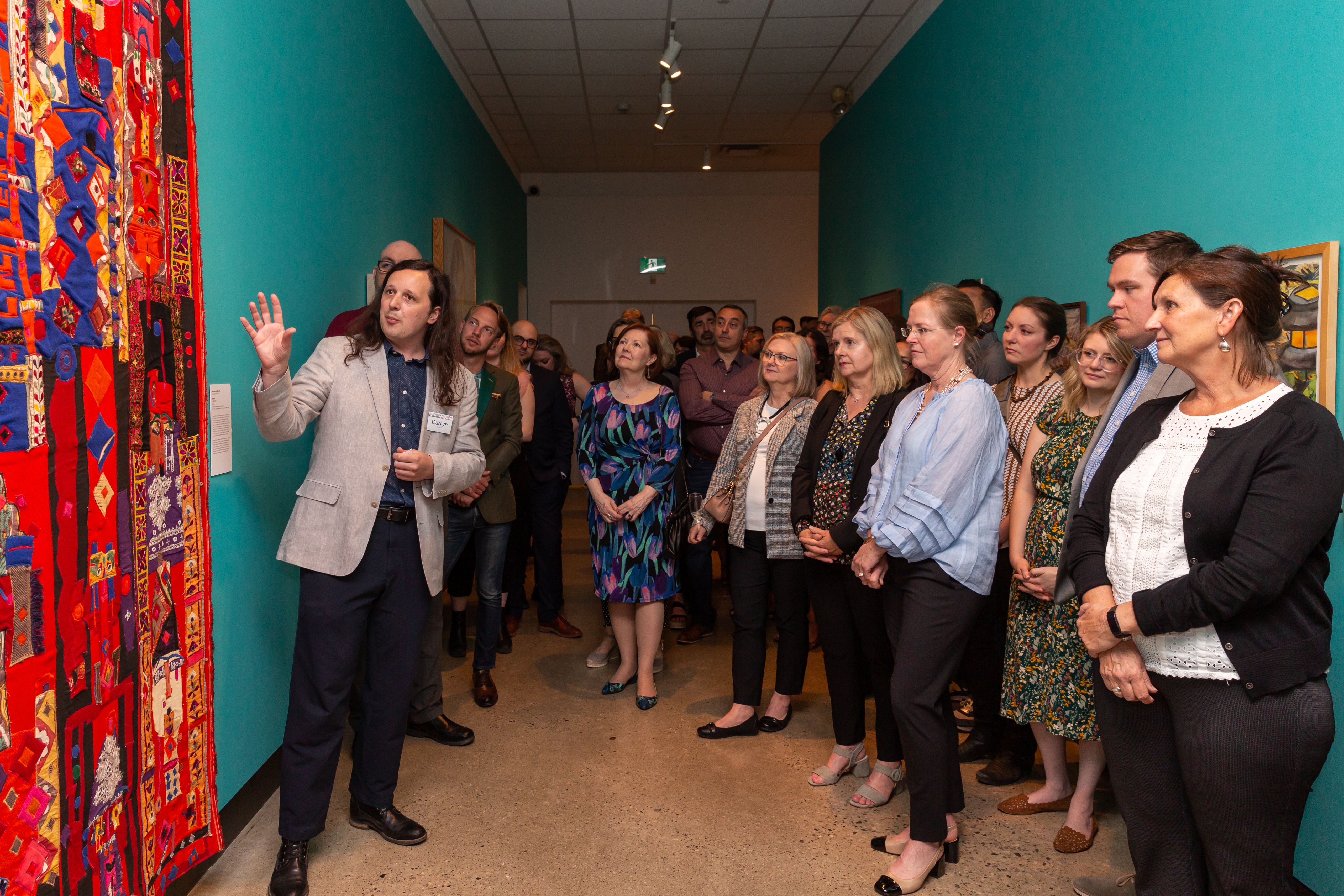 Curator Darryn Doull stands in front of an artwork during an artist talk with an audience in the KWAG corridor