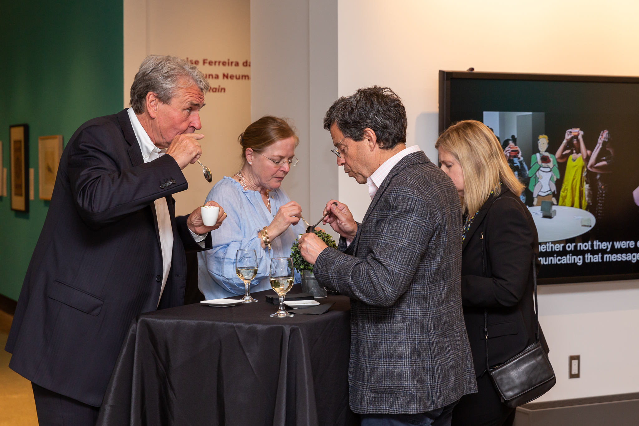 Group of three people standing around a tall cocktail table eating desserts in the background of the KWAG lobby