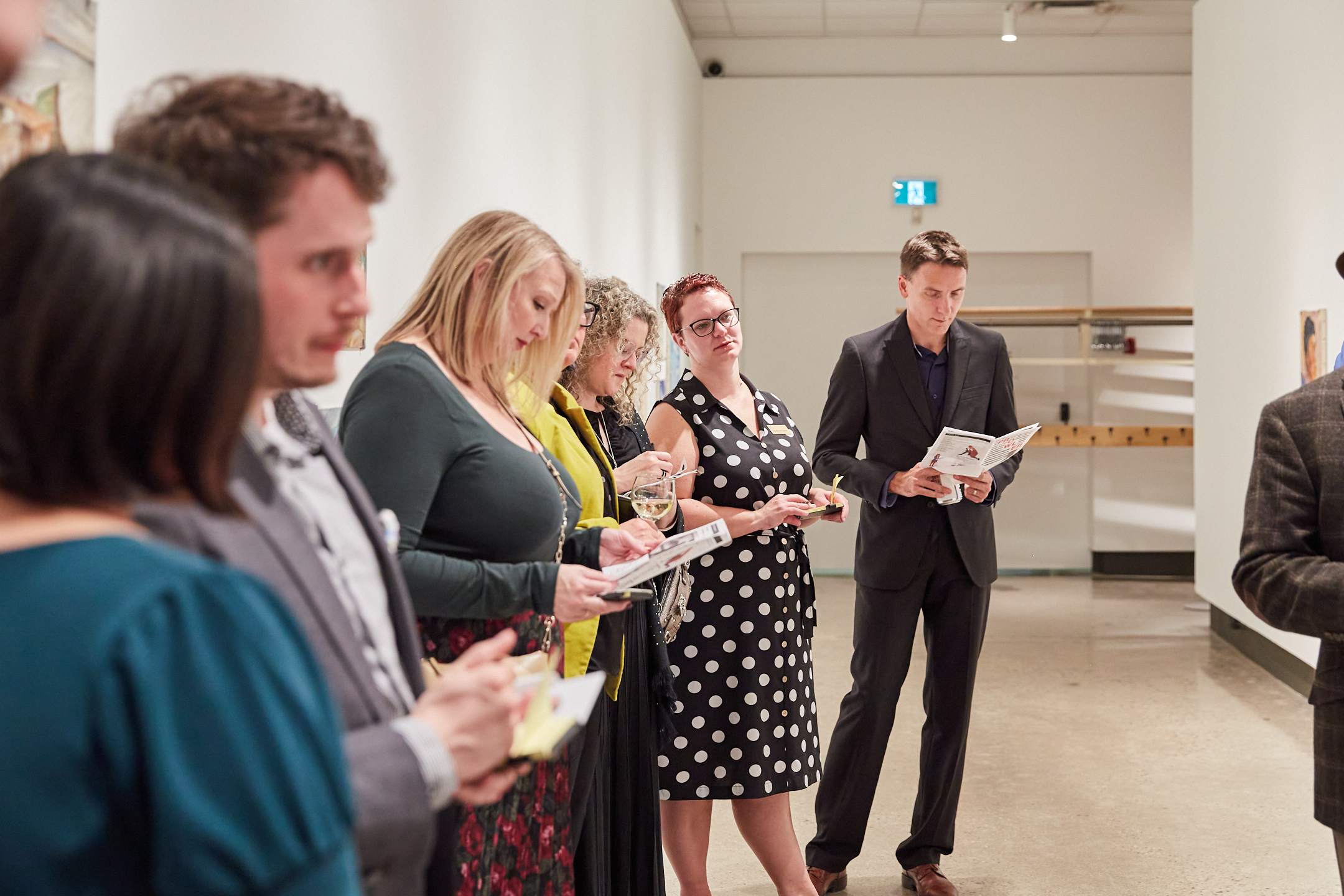 Group of people gathered to the left side of a corridor. Each person holds reading material.