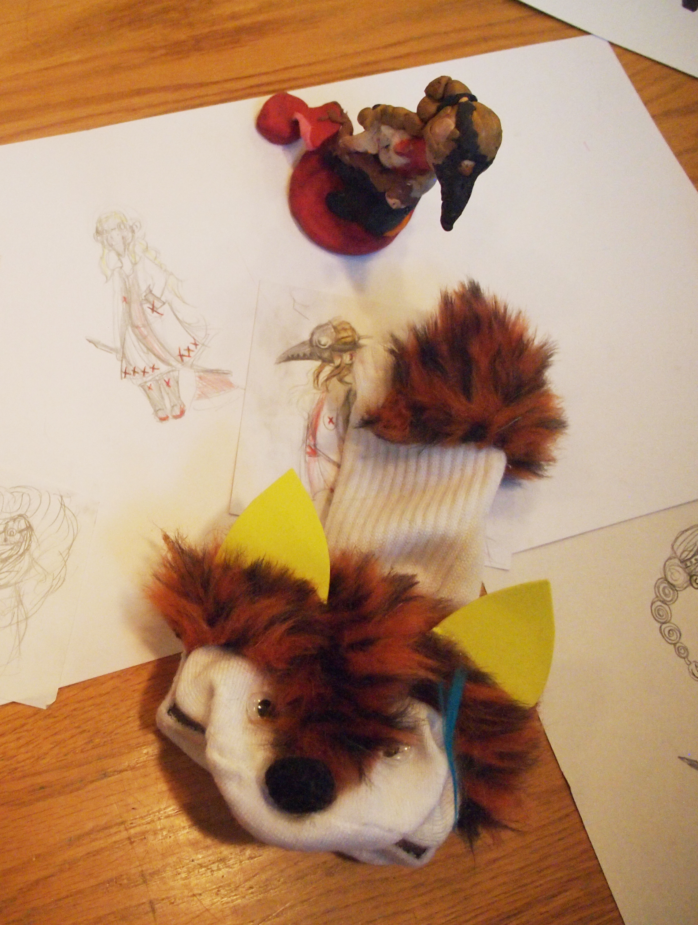 A clay model and sock puppet of characters with animal features rest of top of paper with sketches of more characters