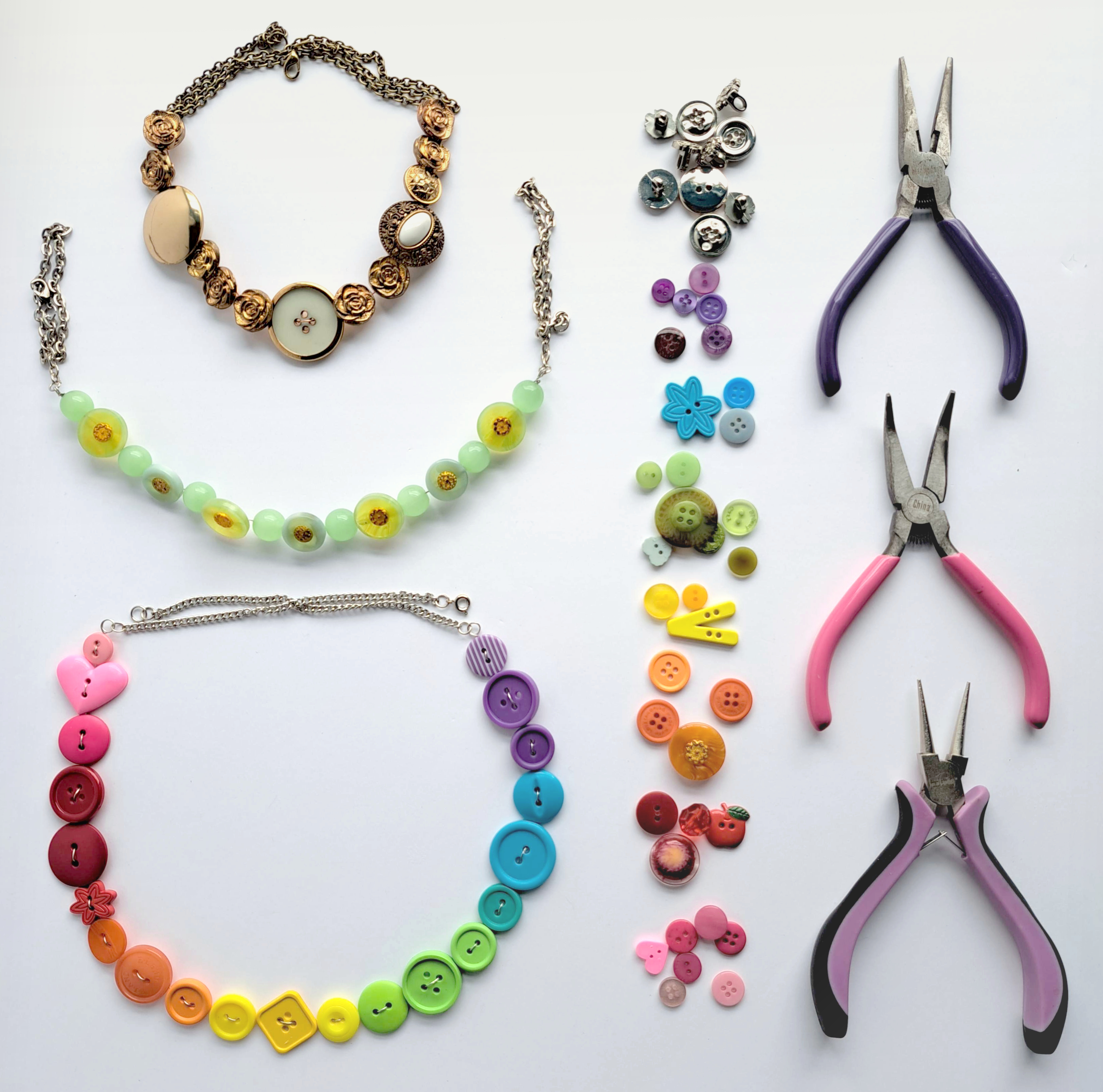 Three necklaces made of buttons, a line of colourful buttons and three pliers for jewelry making.