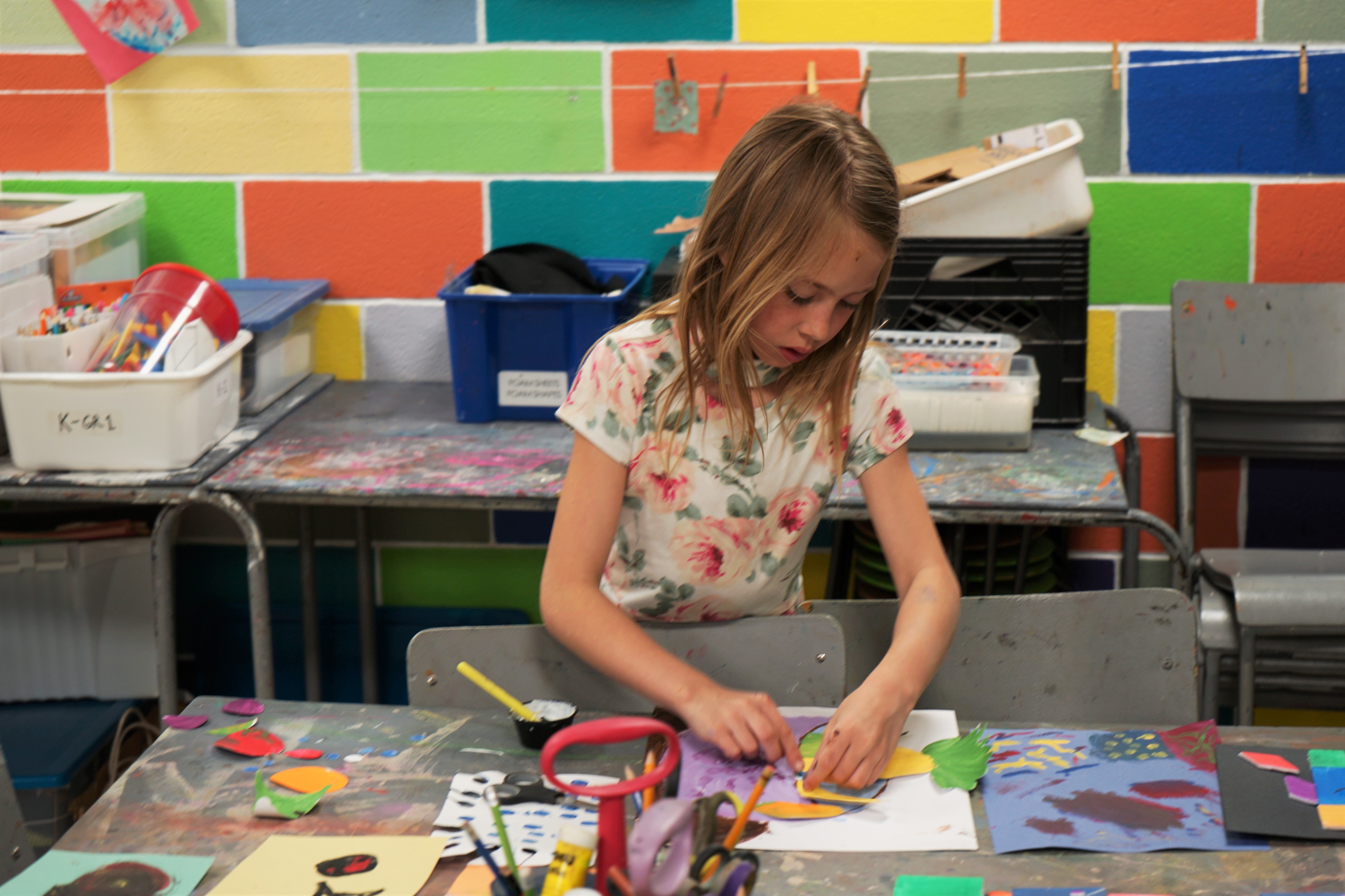 Young girl standing behind a table working on a collage of coloured paper