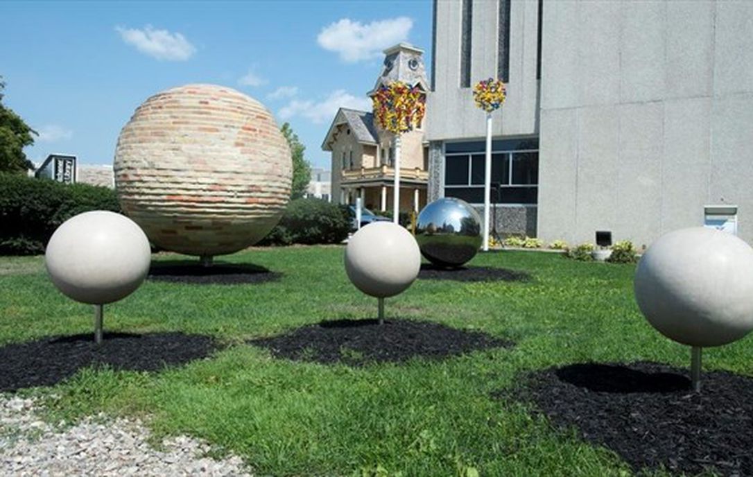 Outdoor sculptural arrangement of various spheres mounted on thin posts on a green lawn