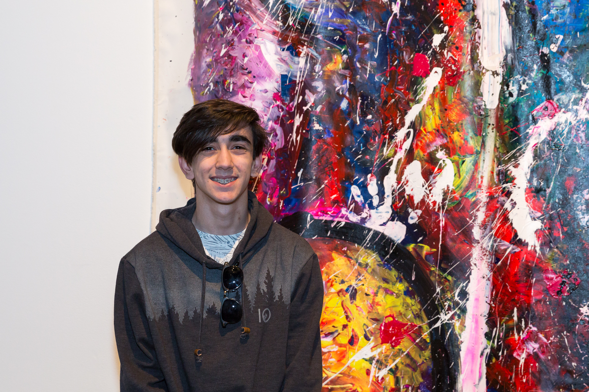 A teenage boy stands smiling in front of a large-scale abstract painting hanging in a white-walled gallery