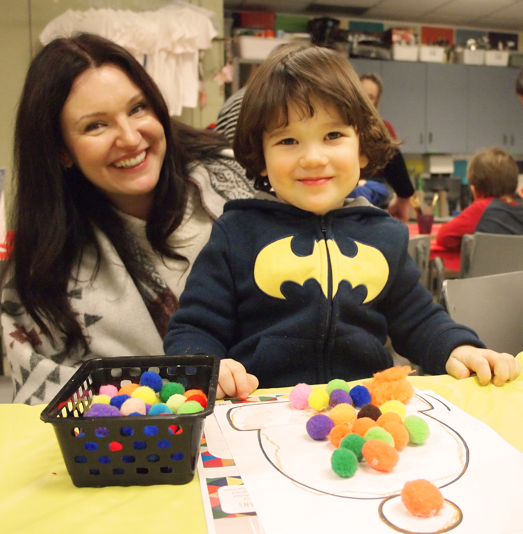 Photo of a smiling young boy and his mother making a pom-pom snowman