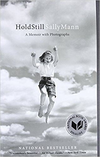 Cover of Sally Mann's Memoir Hold Still featuring a black and white photo of a girl leaping against an open but cloudy sky