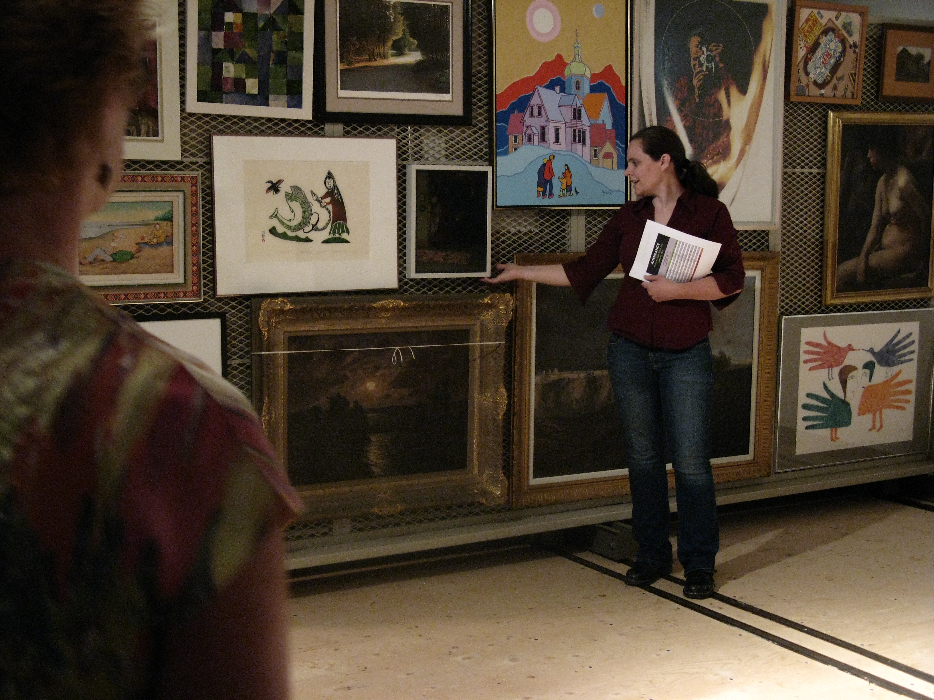 Gallery Registrar Jennifer Bullock gestures to one painting among many hung salon-style on a rolling rack in the vaults during a tour