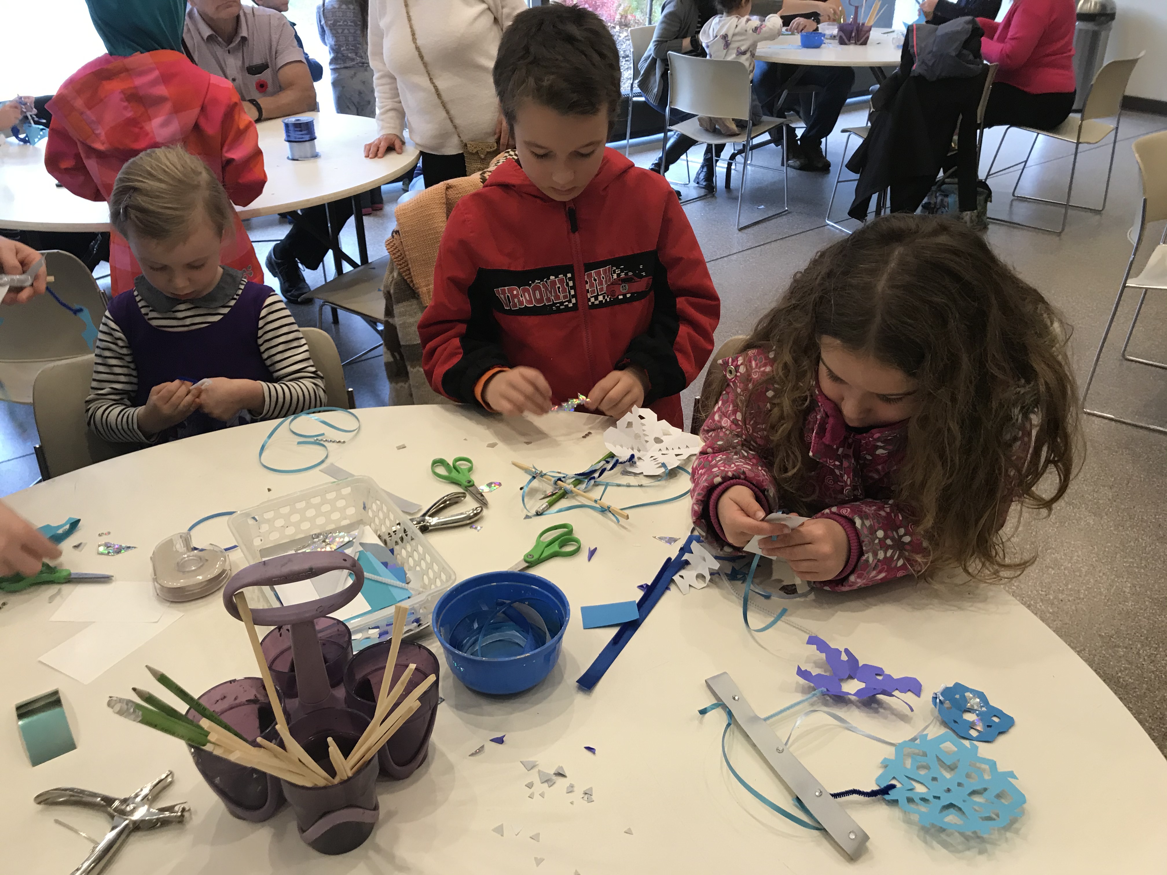 A group of children seated at a table making paper snowflakes