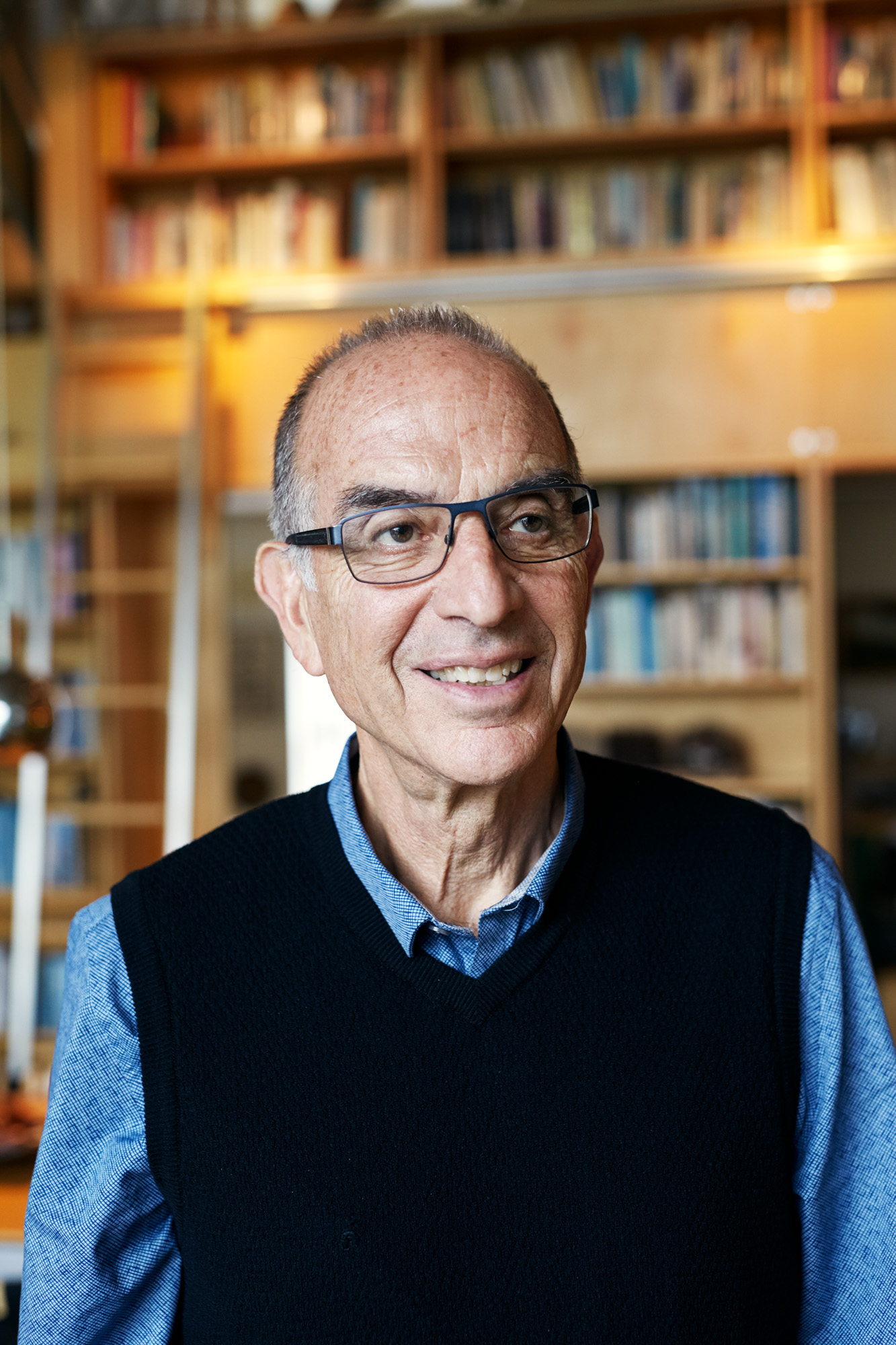 Photo of Ken Greenberg, an older man wearing glasses and a black sweater vest over a blue shirt