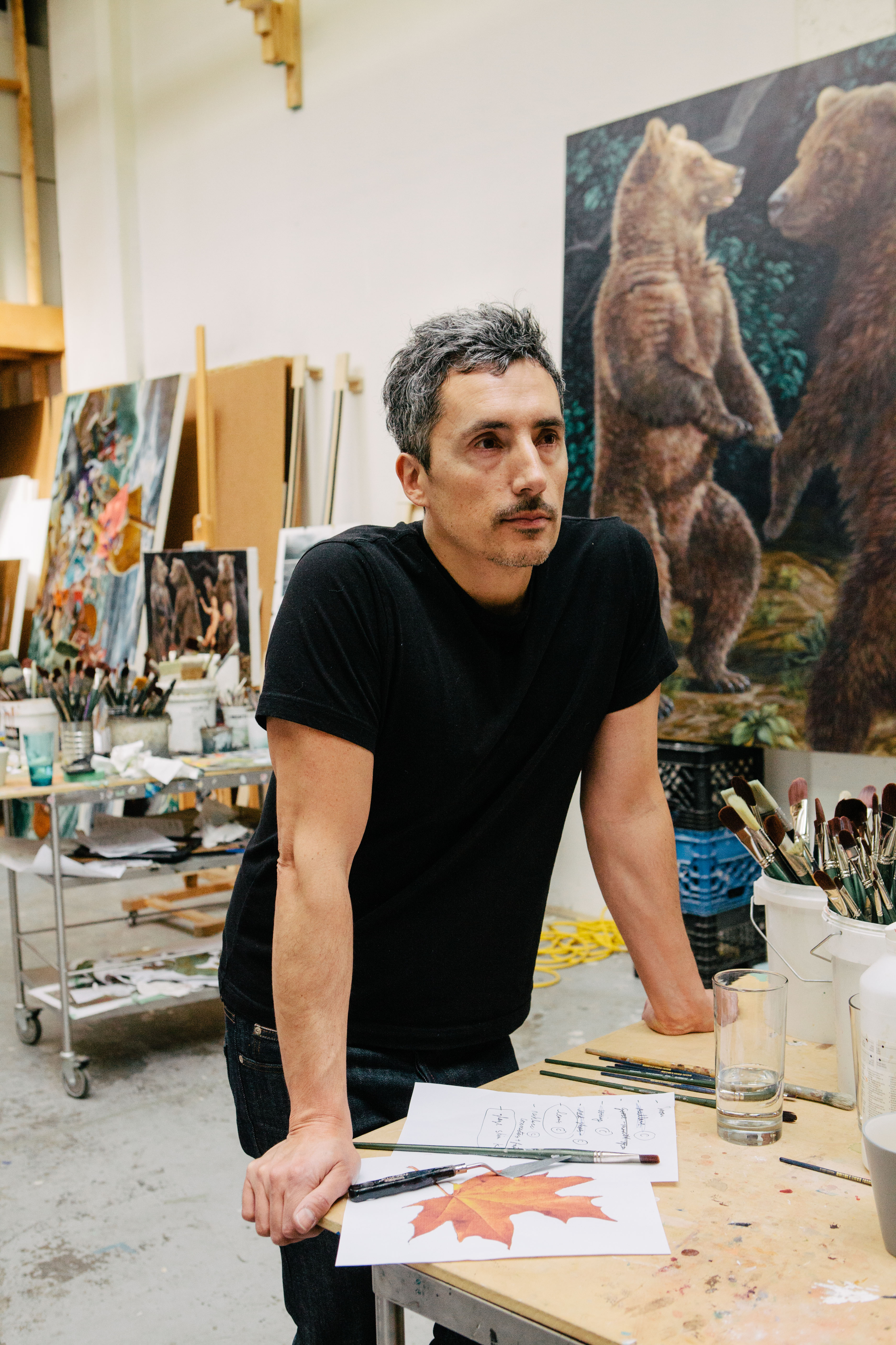 Photo of Kent Monkman leaning against a work table in his studio