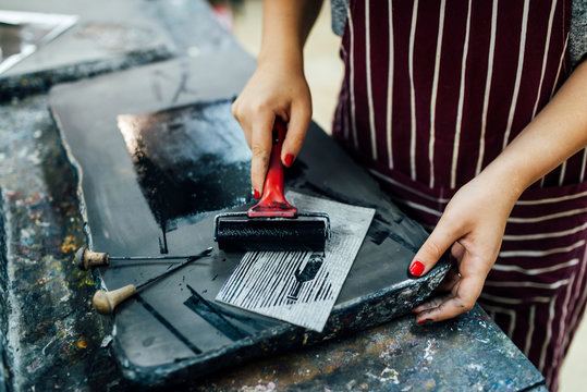 A woman's hands with red nail polish rolling black ink on a block print