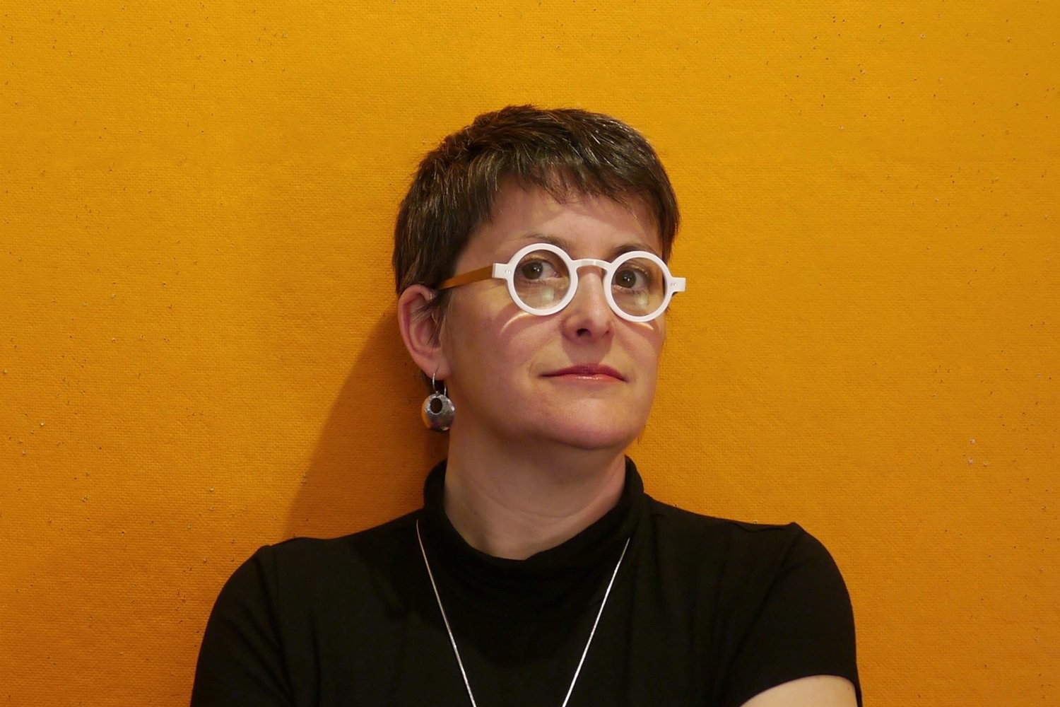 Photo of Lisa Rapoport, a woman with white round glasses standing in front of a yellow wall.