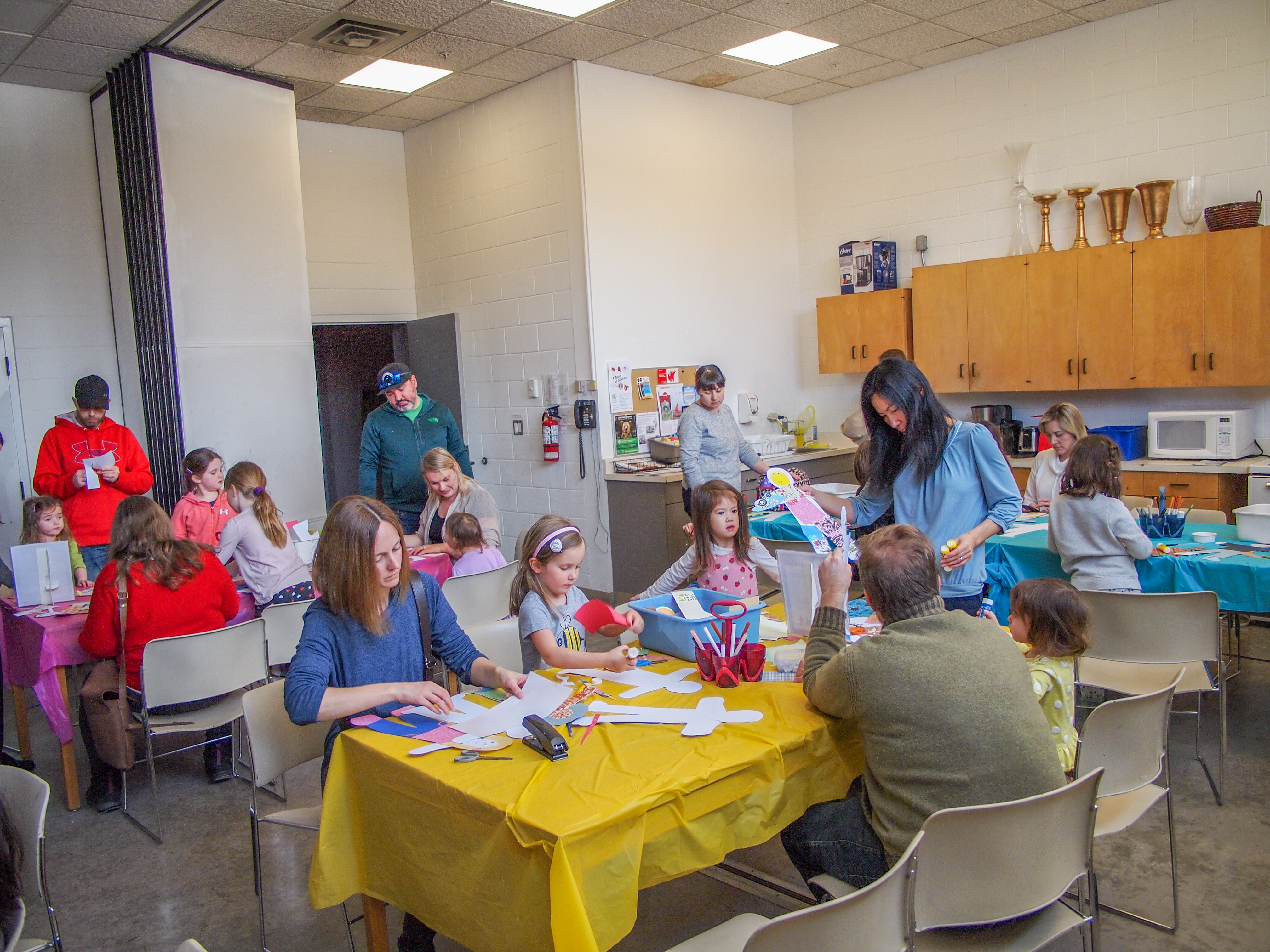 A group of people of various ages around a table with art supplies/