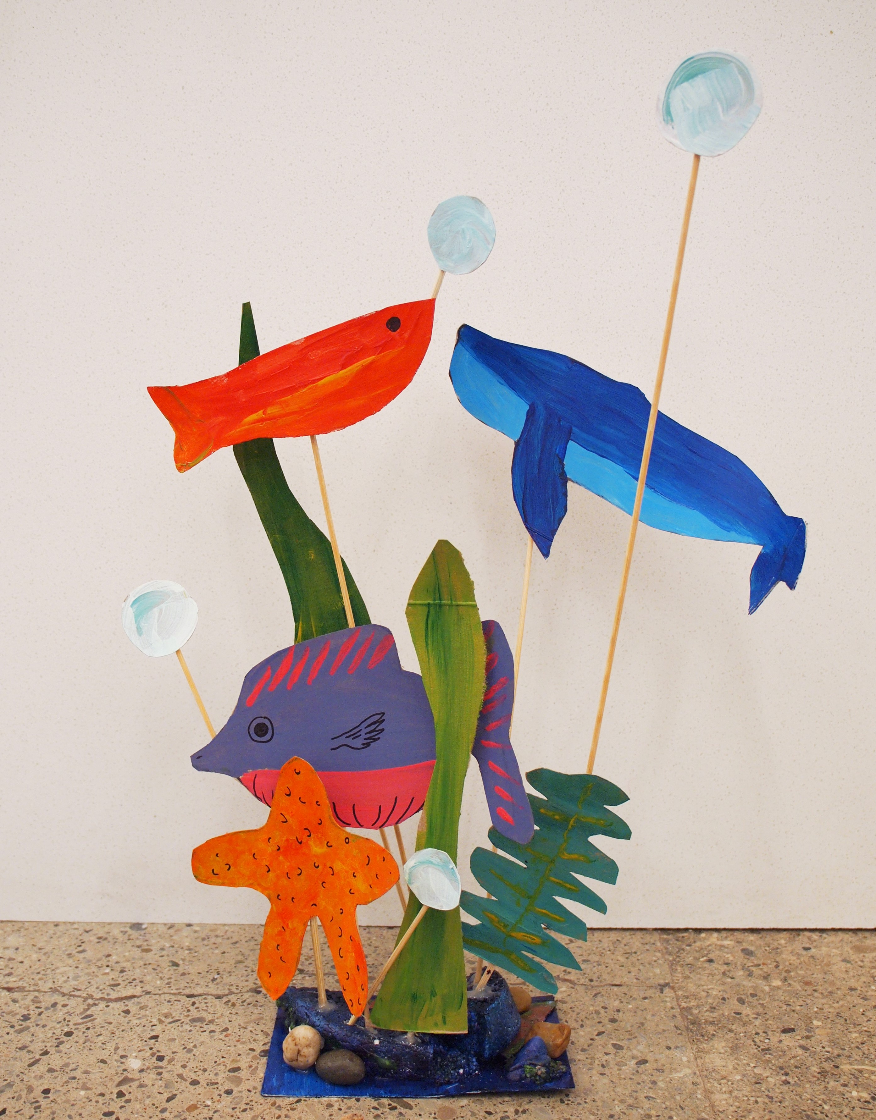 Photo of a painted paper sculpture of fish and whales suspended on wooden skewers