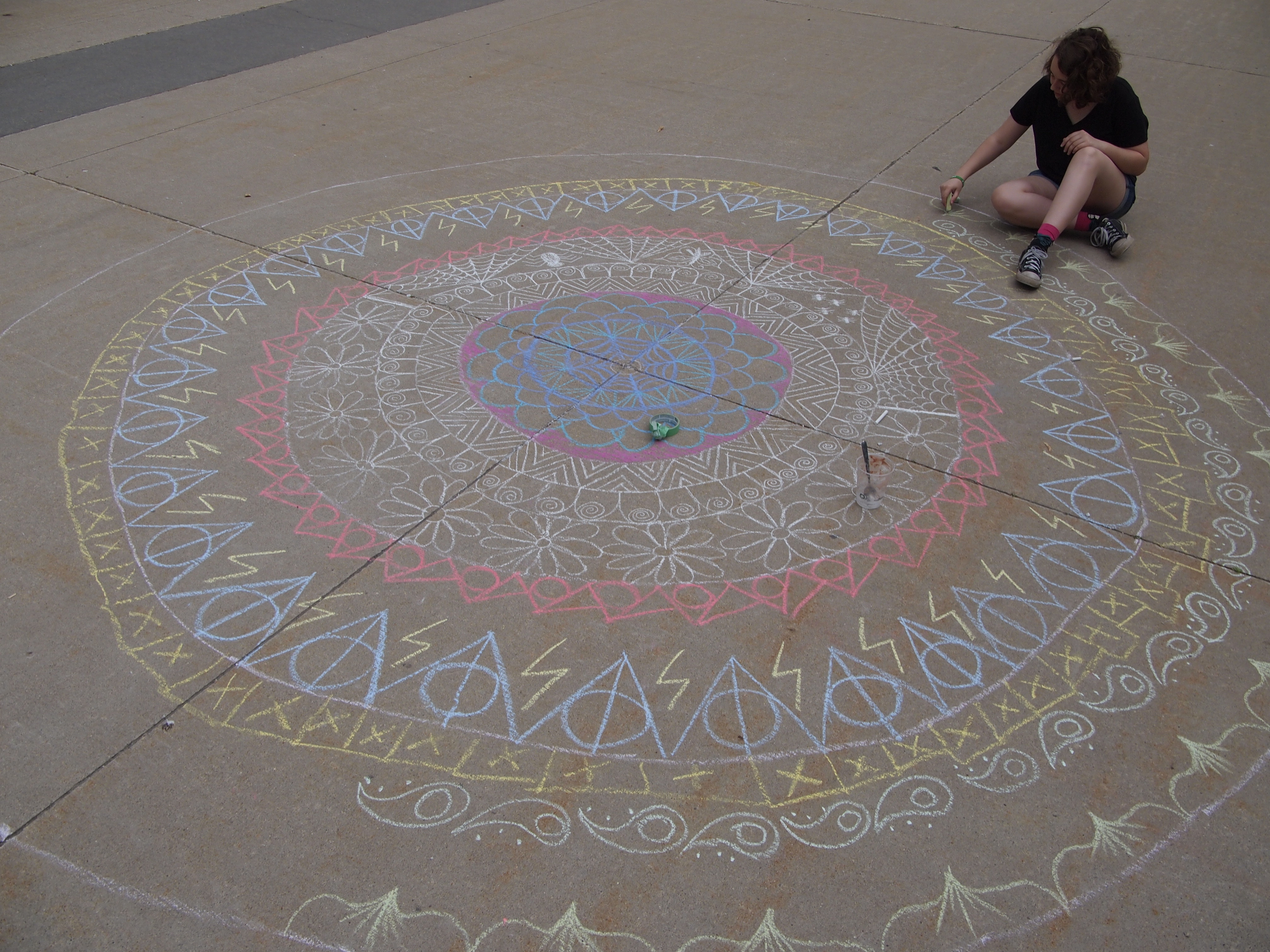 Overhead photo of a young girl drawing a large chalk mandala on the concrete outside Centre In The Square