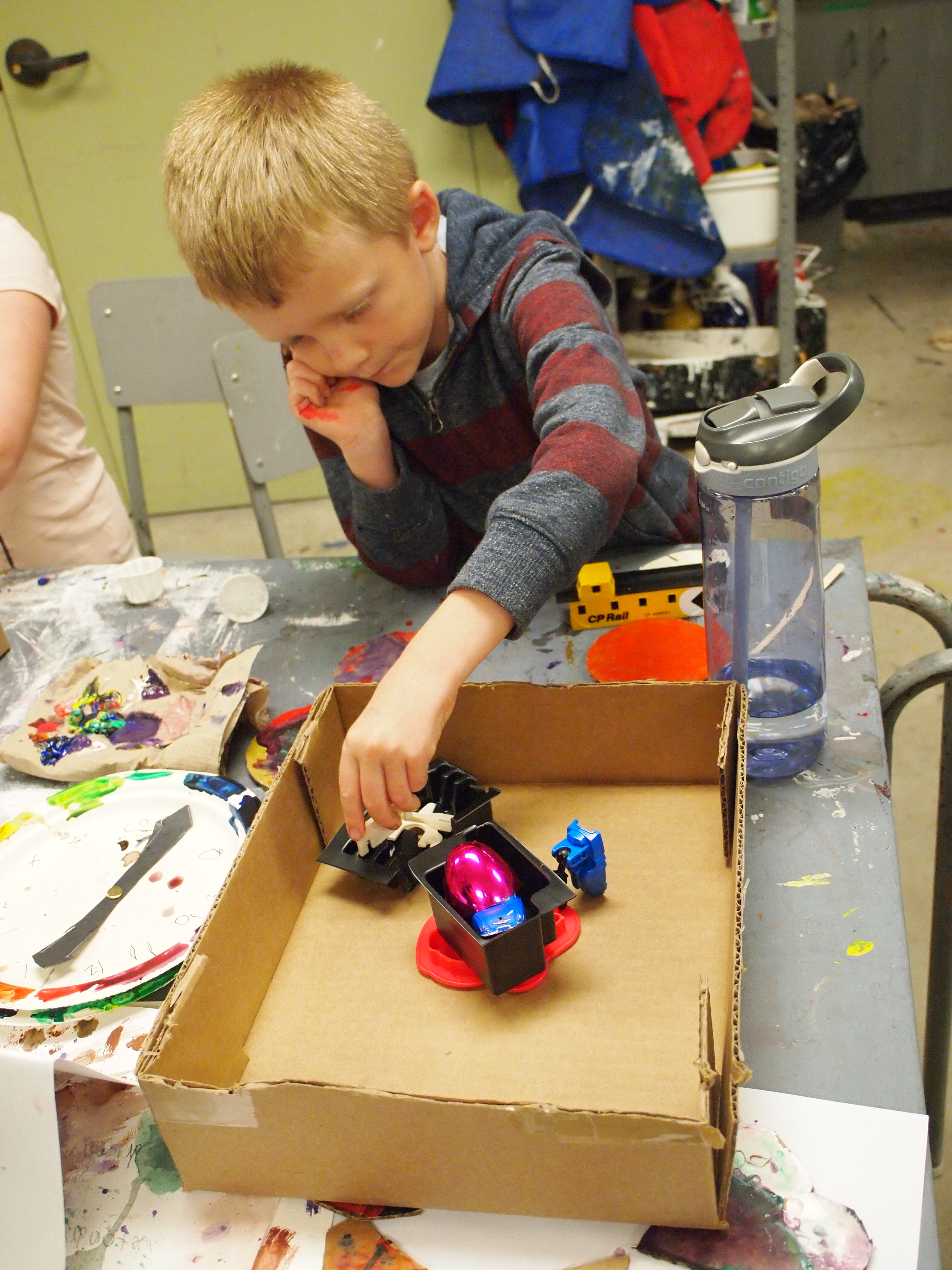 A young boy looking thoughtful as he places objects in a colourful abstract construction set inside a shallow cardboard frame