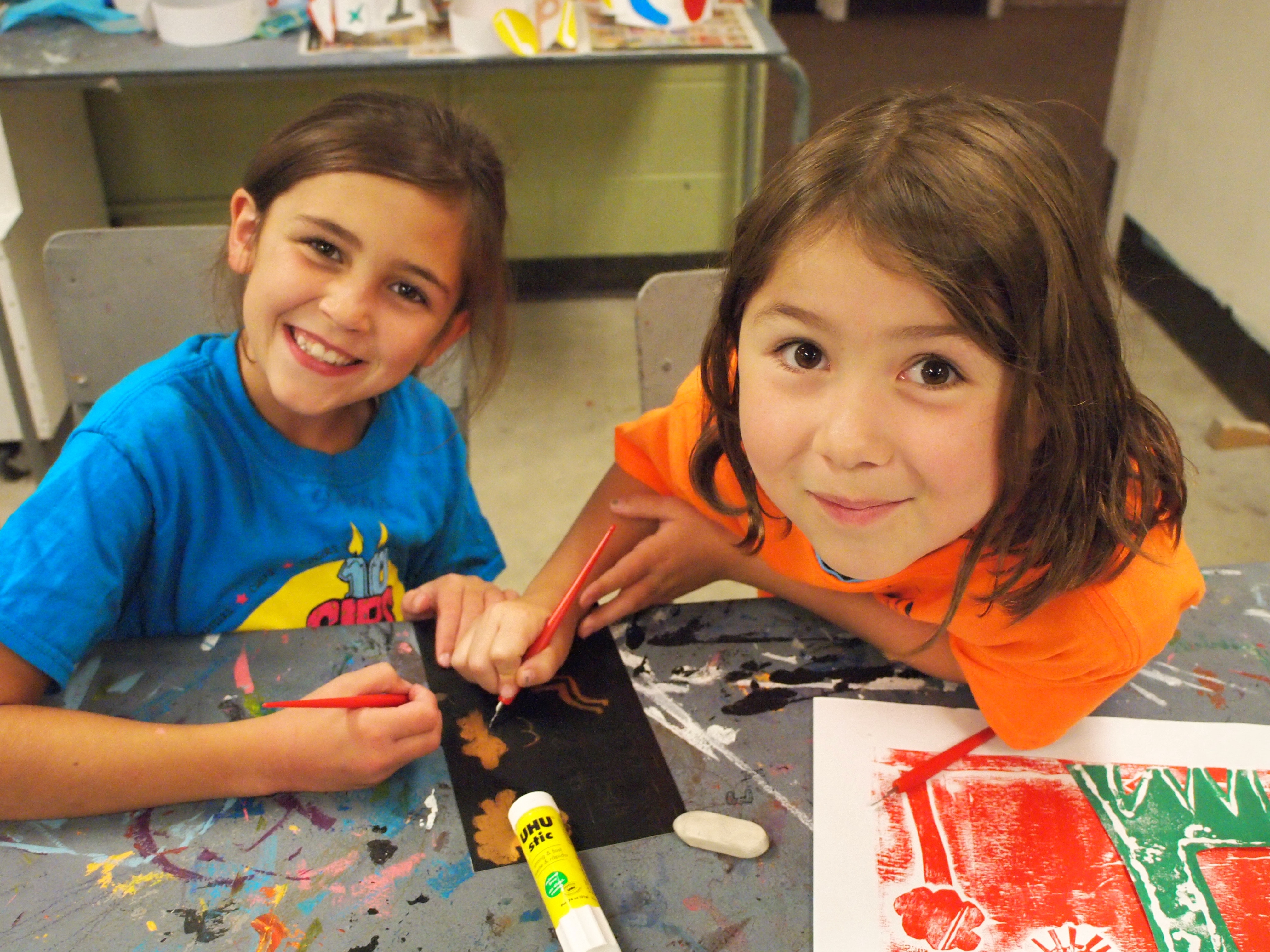 Two young girls peer up happily from their paintings in the KWAG studio