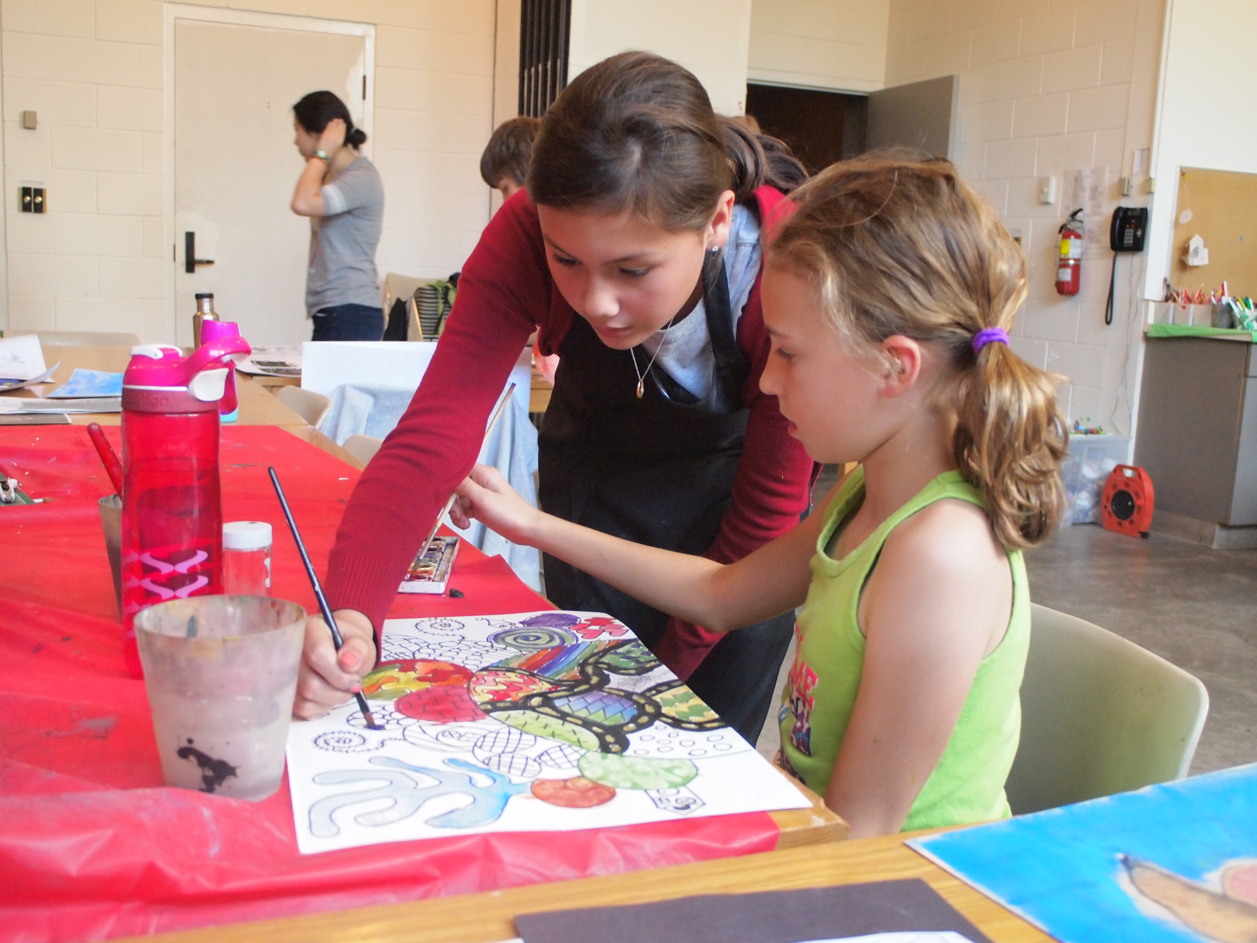 Two girls at a table in the KWAG studio working together on a colourful patterned drawing