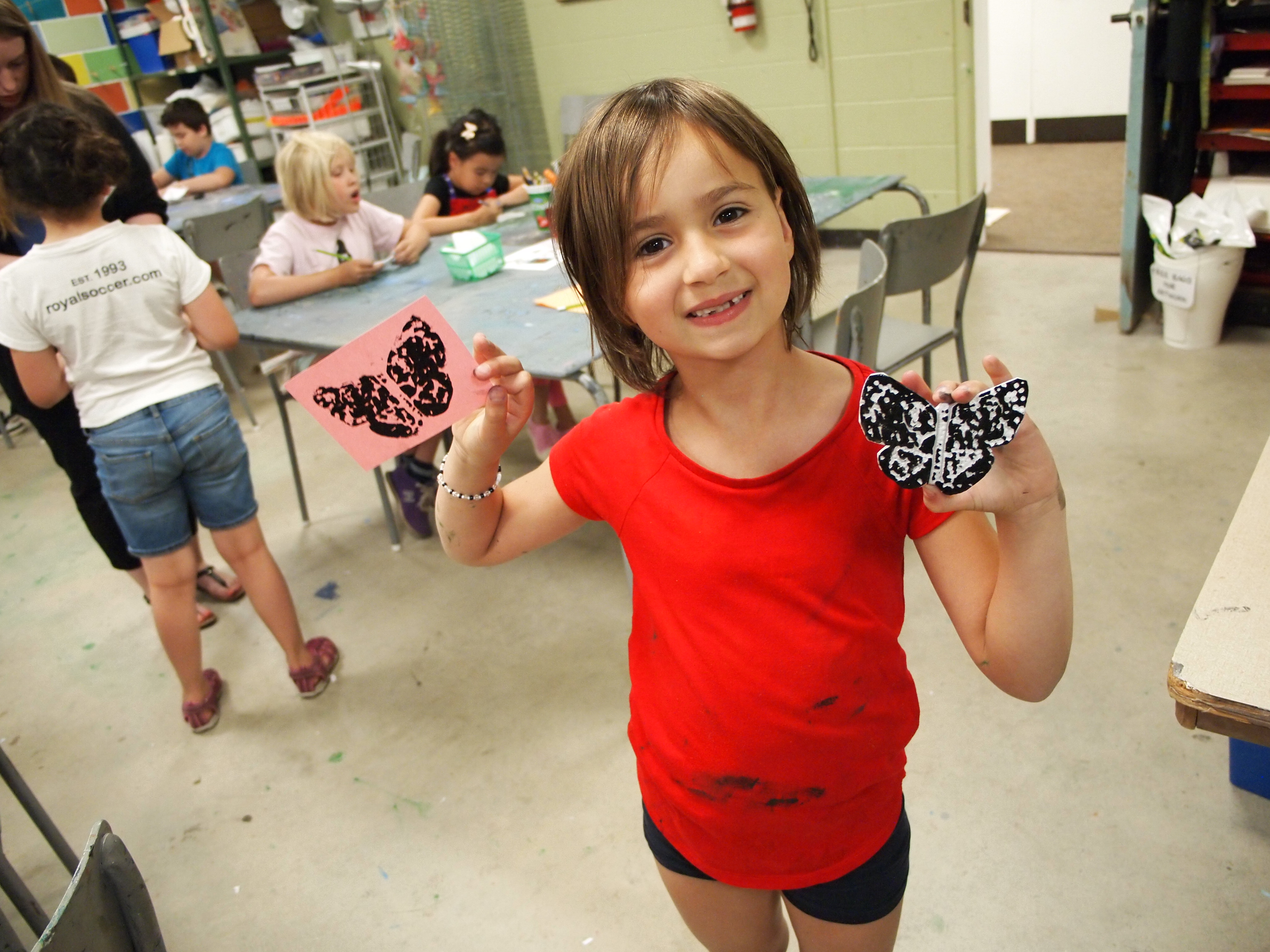 Child smiling at camera holding up a print of a butterfly