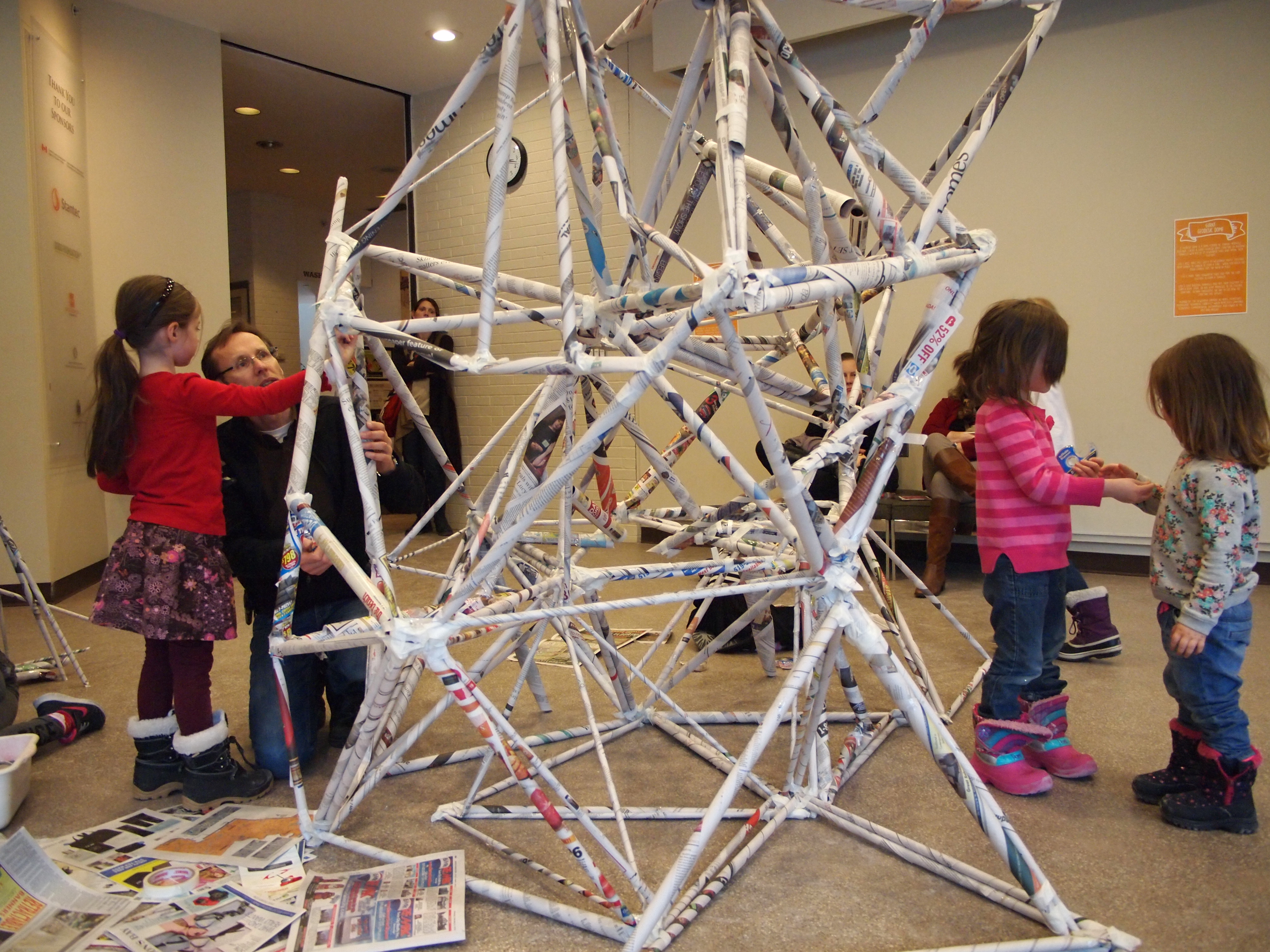 A small group of children and their parents work together to create a large collaborative geometric sculpture at a KWAG Family Day event