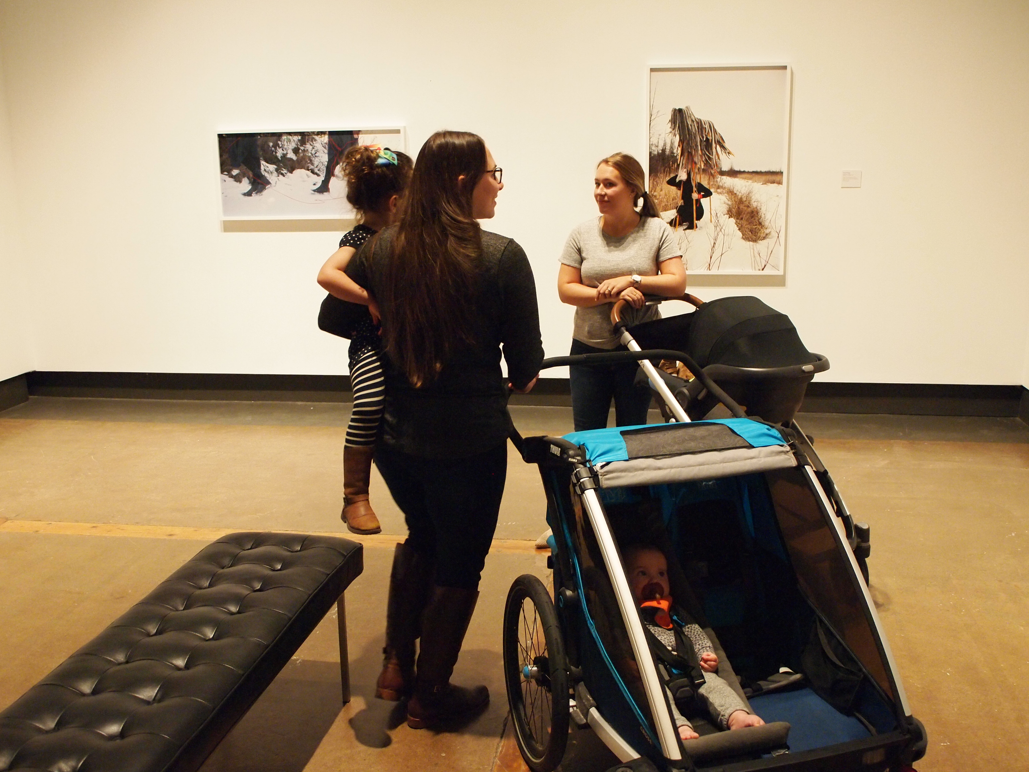 Two mothers with strollers carrying young babies smiling and chatting together in the gallery