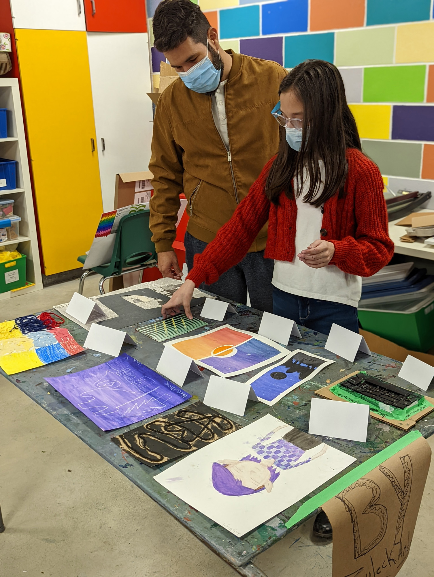 A young girl uses a brush to touch up a print in progress of repeating black bird patterns with printmaking tools laid out around her work space