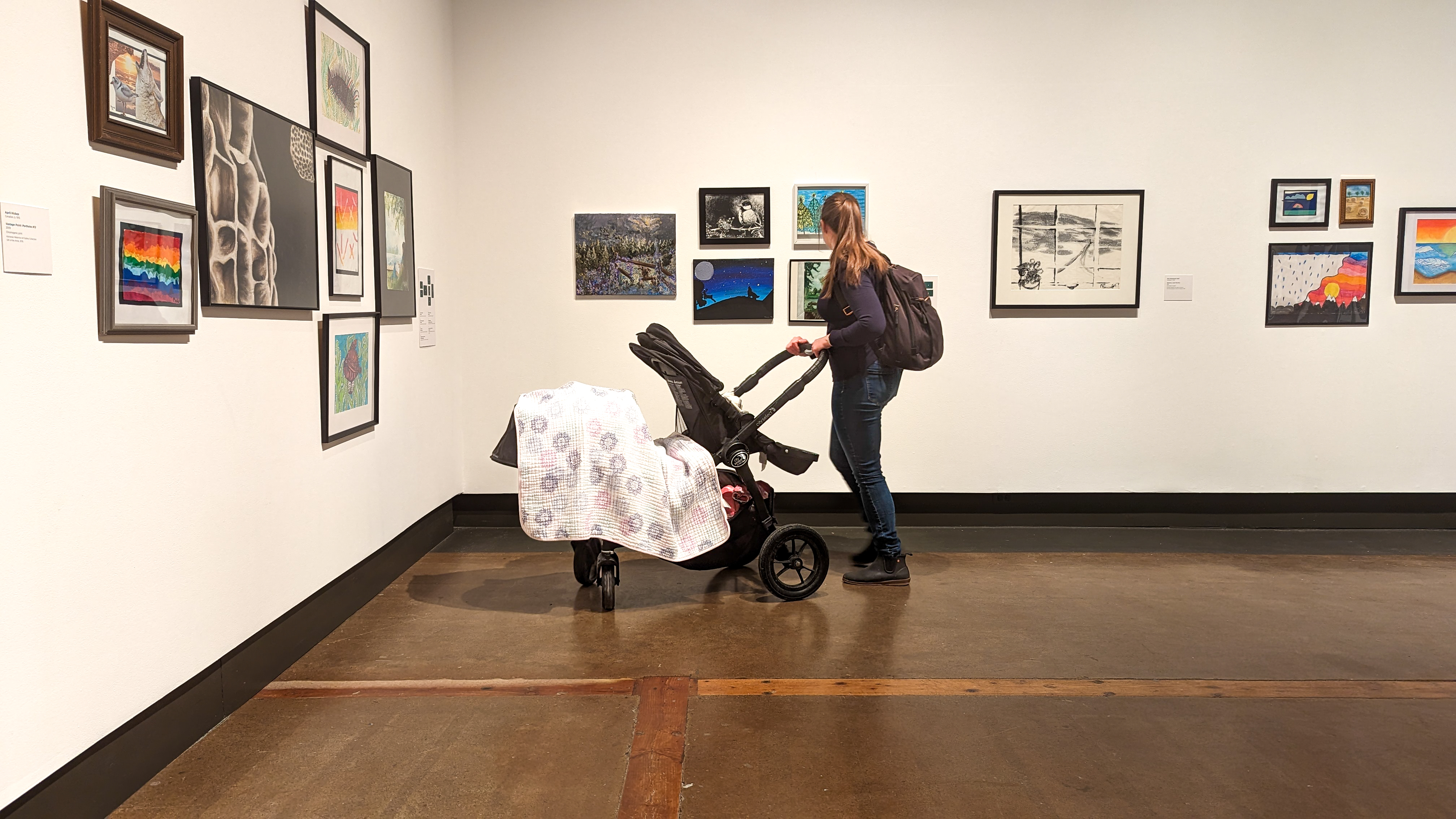 A mother with a stroller standing looking at paintings and drawing on the wall