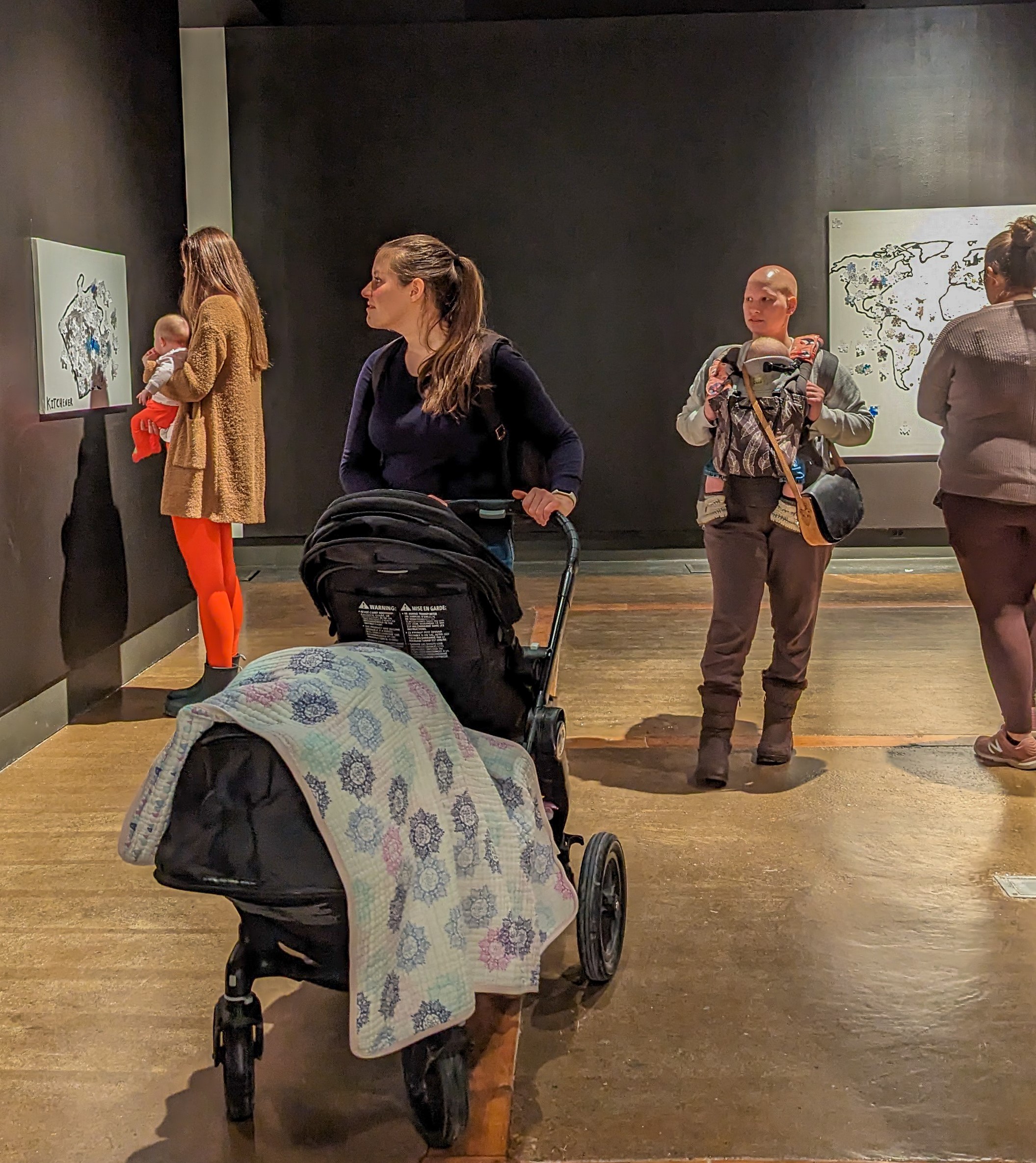 A mother with a stroller standing looking at paintings and drawing on the wall