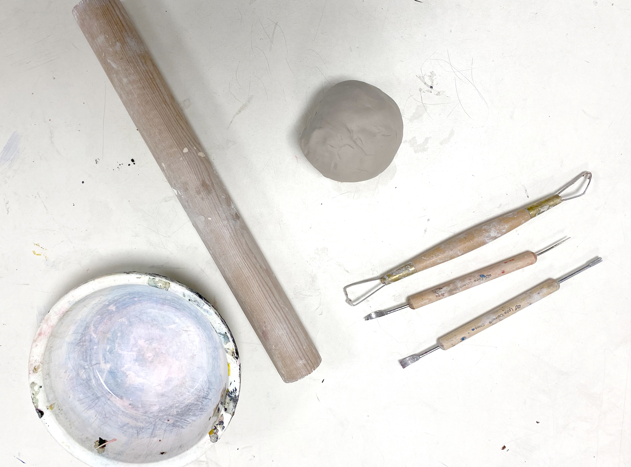 A small ball of clay on a white table top surrounded by pottery tools