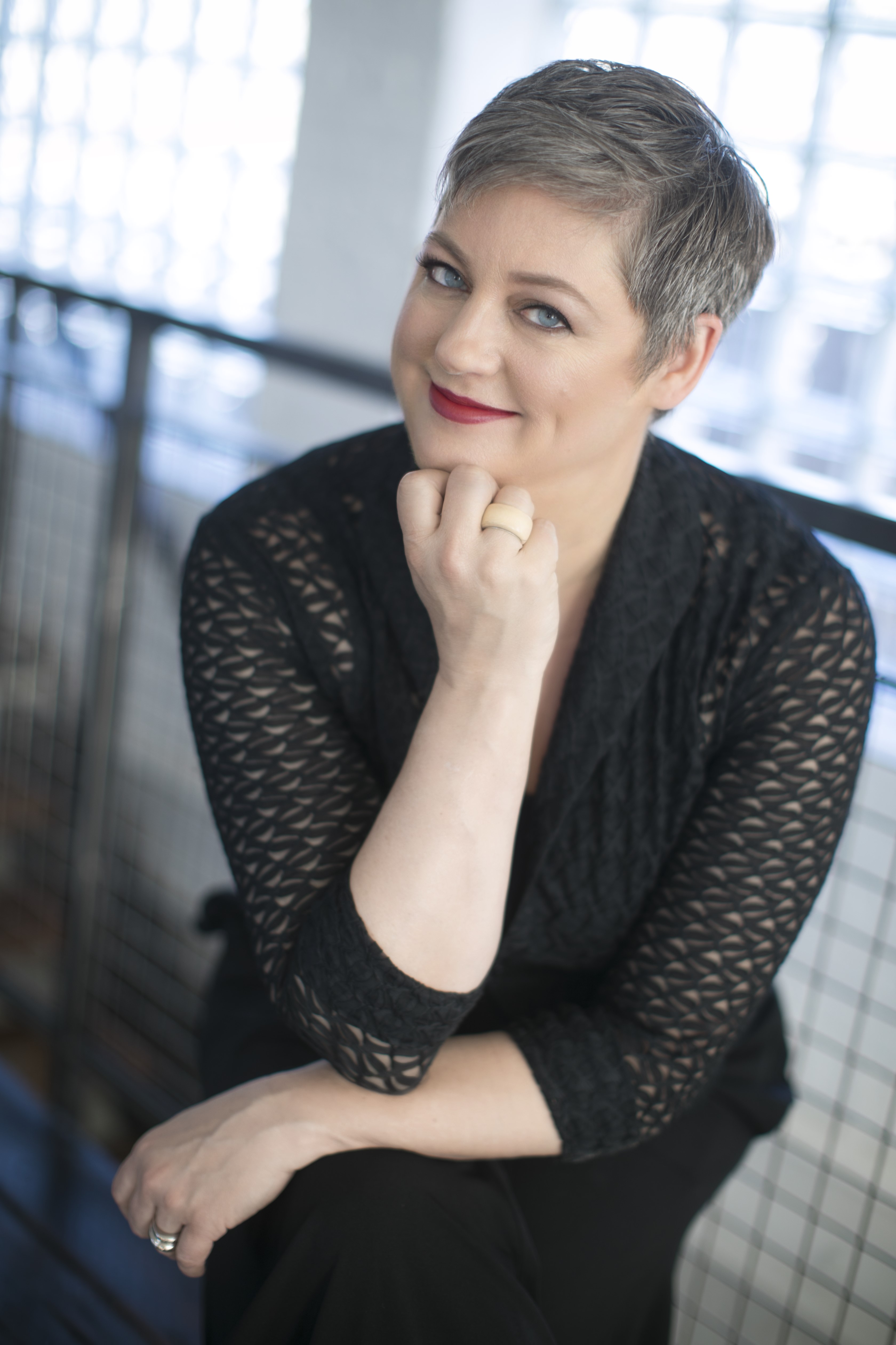 Photo of Heidi Reitmaier, a smiling woman with short grey hair and blue eyes wearing a black geometric lace top