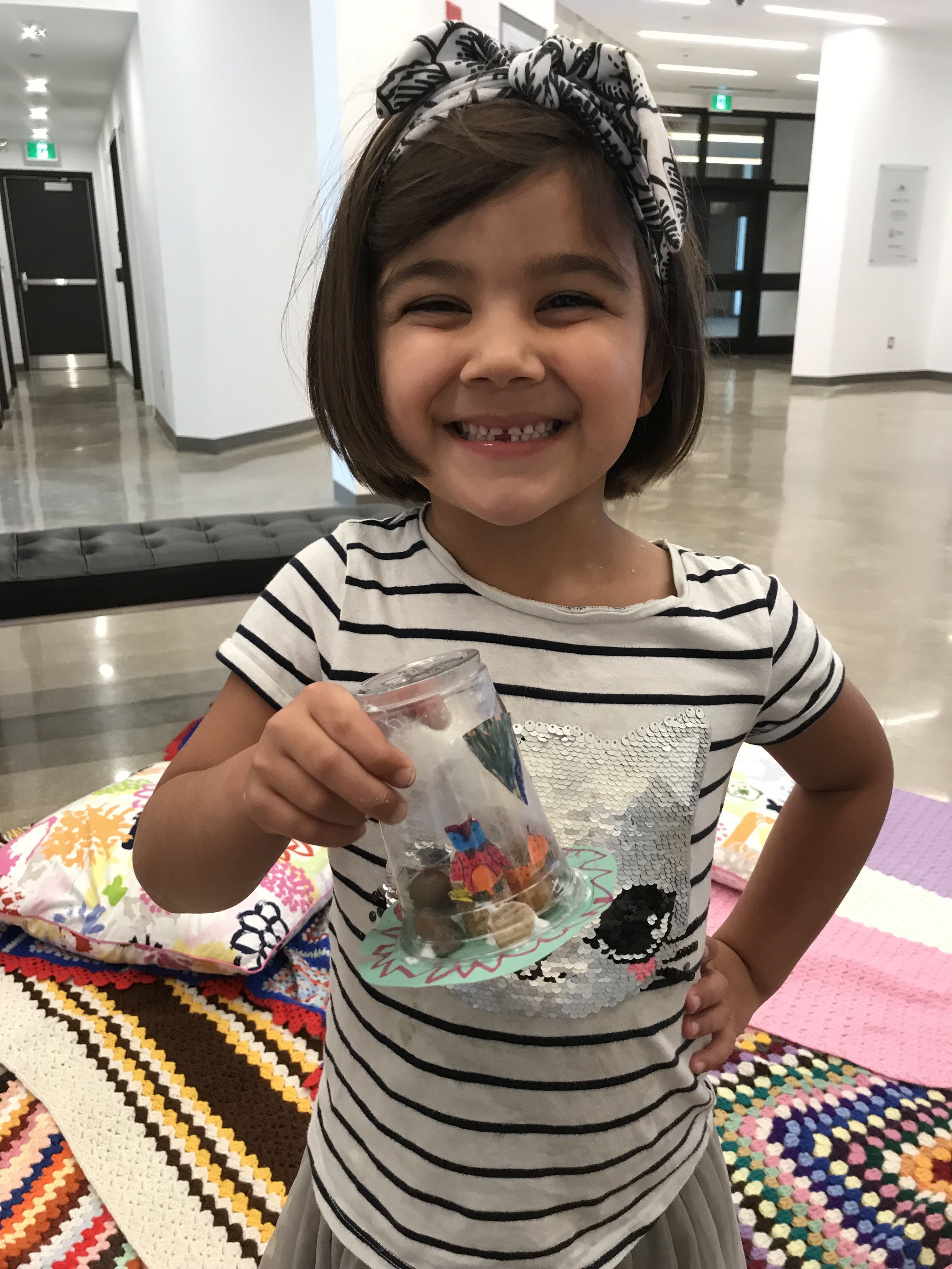 A young girl smiling as she shows off a mini terrarium made from found materials at Family Sunday