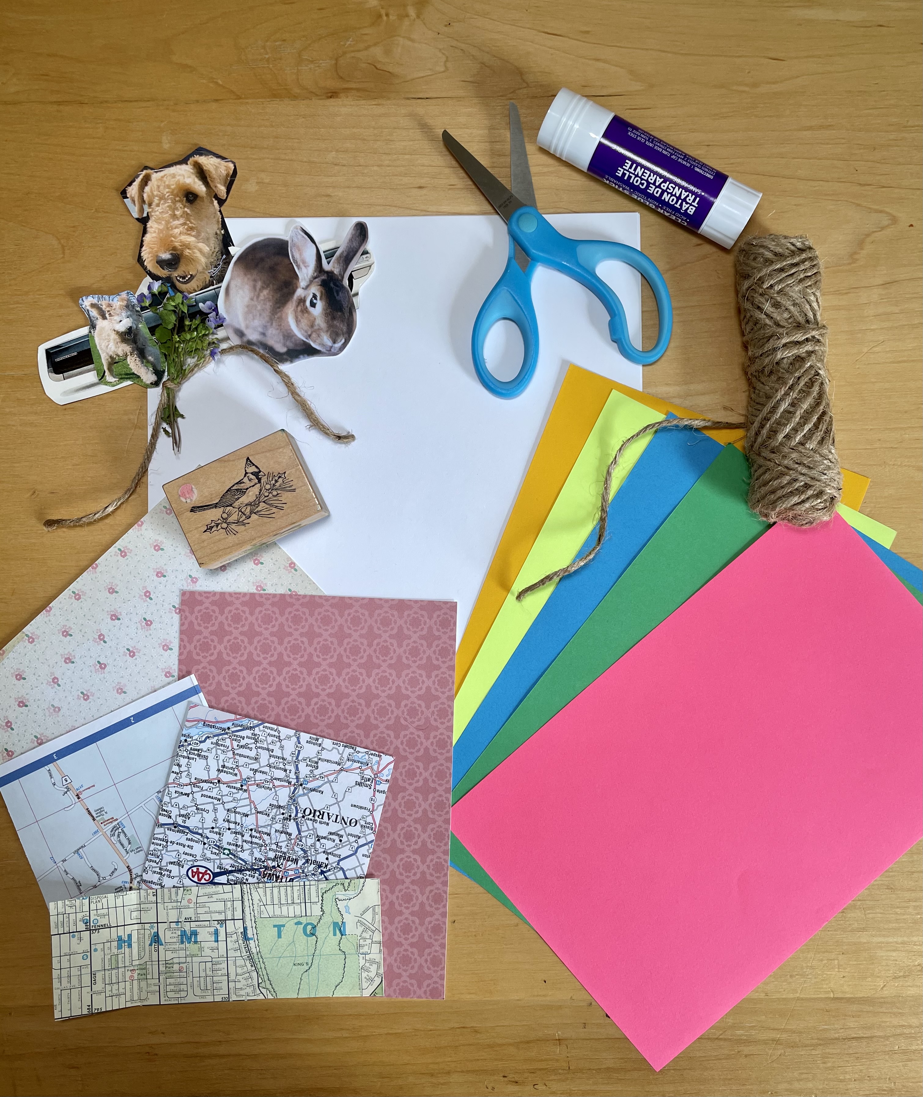 A display of collage materials including coloured and patterned paper, cut-out images of animals, a rubber stamp, scissors, glue and string