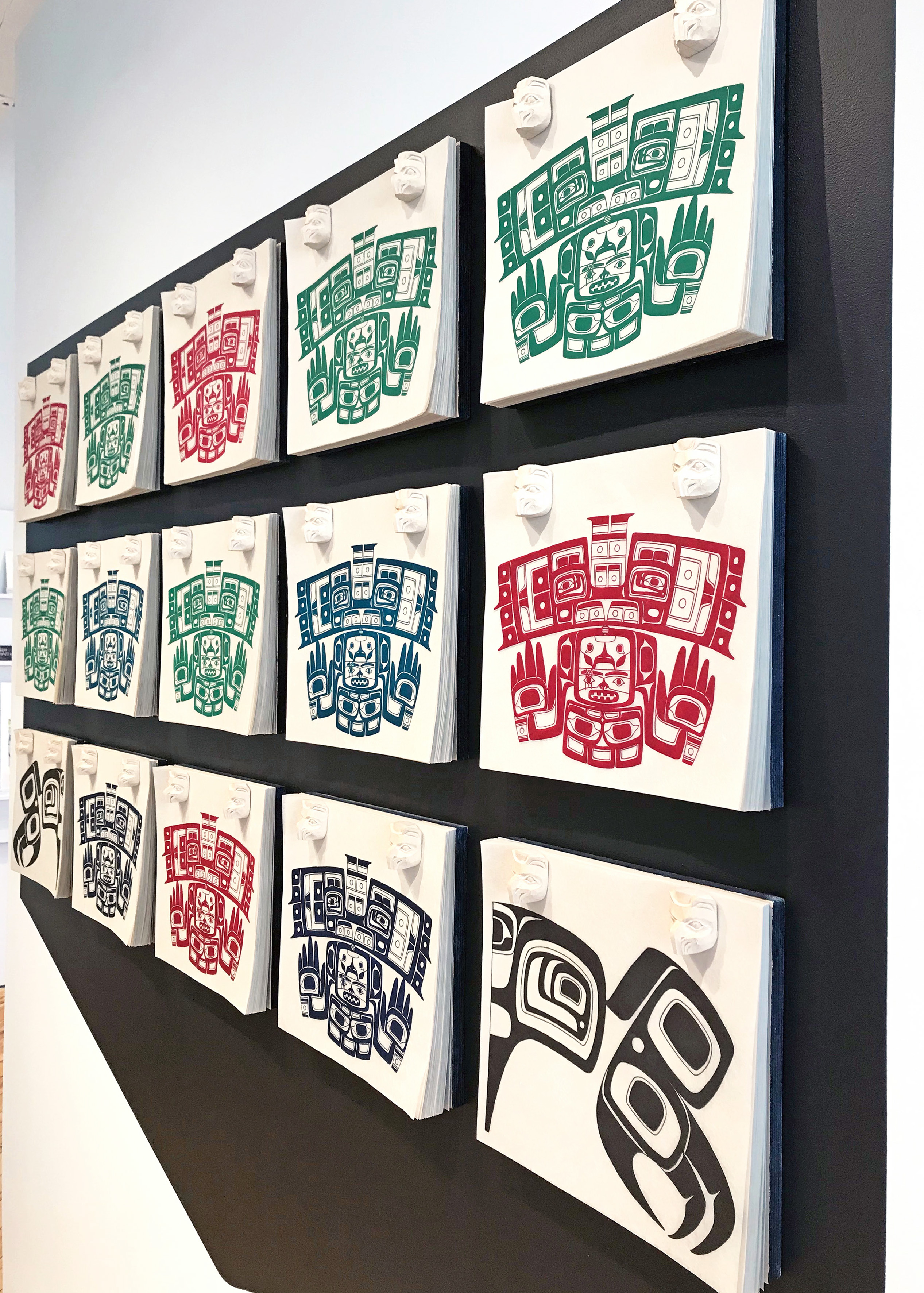 A sidelong view of Luke Parnell's installation of lithograph prints based on Northwest coast Indigenous Chilkat blankets stacked in hanging grids against a black background