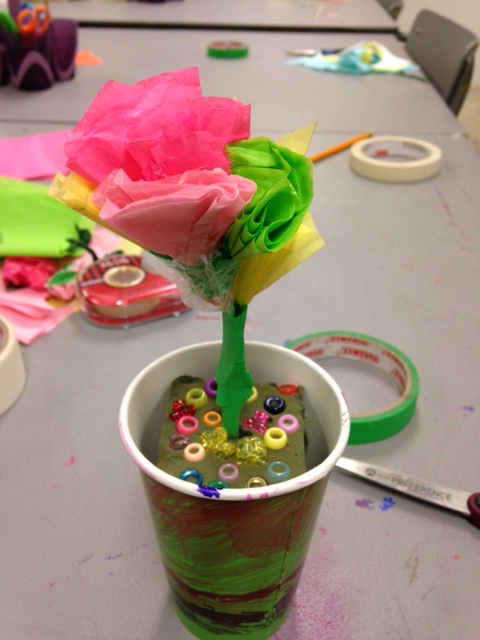 A tissue paper flower sits upright in a painted paper cup supported by foam and beads