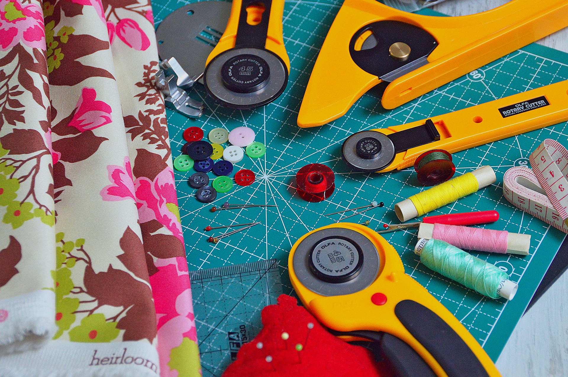 An array of fabric, cutters, buttons and needles on a cutting mat