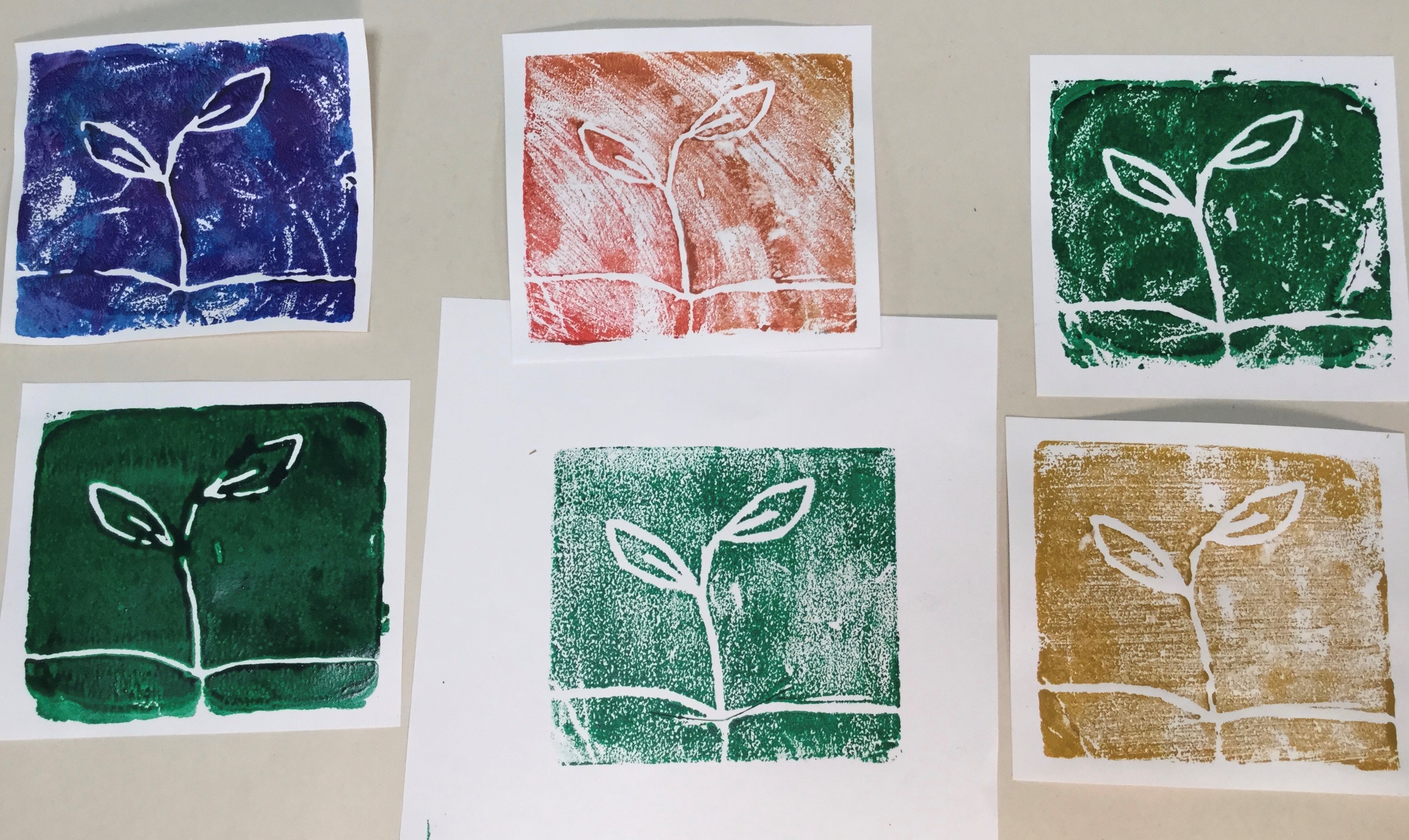 A group of six single-colour block prints of a simple seedling drawing laid out in a grid on a grey table