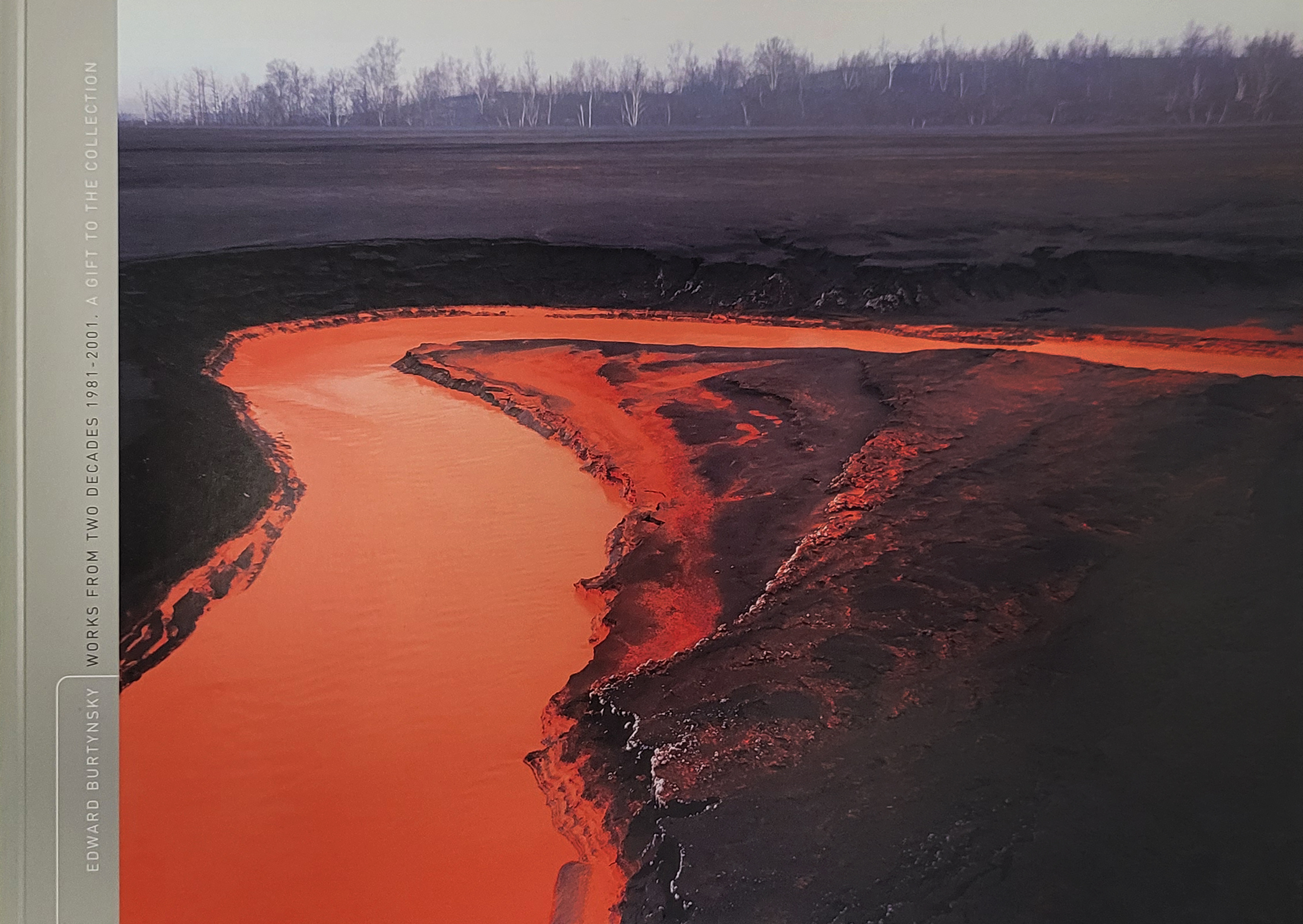 Scan of the book cover featuring a river of vibrant red nickel waste tailings curving around dark mounds of earth