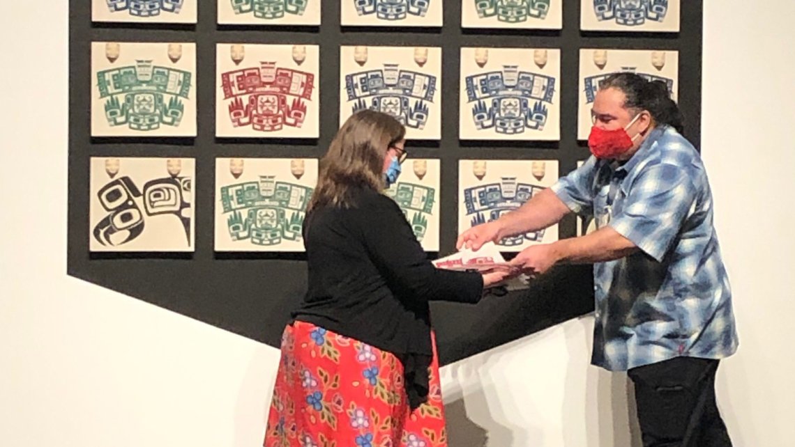 Luke Parnell hands a print from his installation to a woman in a black top and red skirt