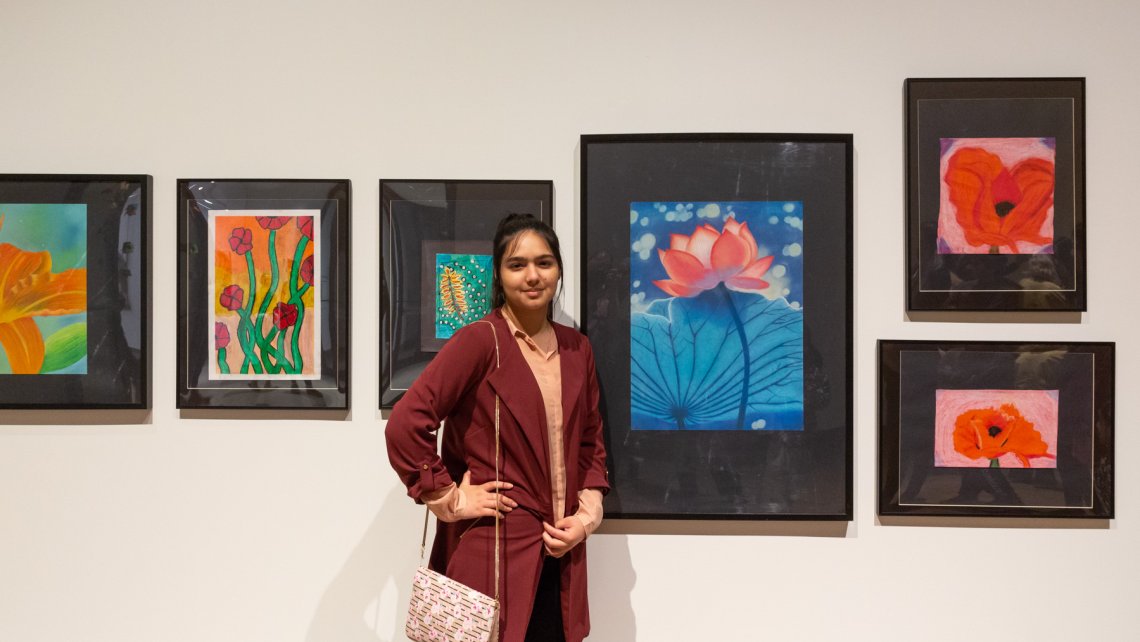 Young person standing in fromt of a white wall filled with student artwork