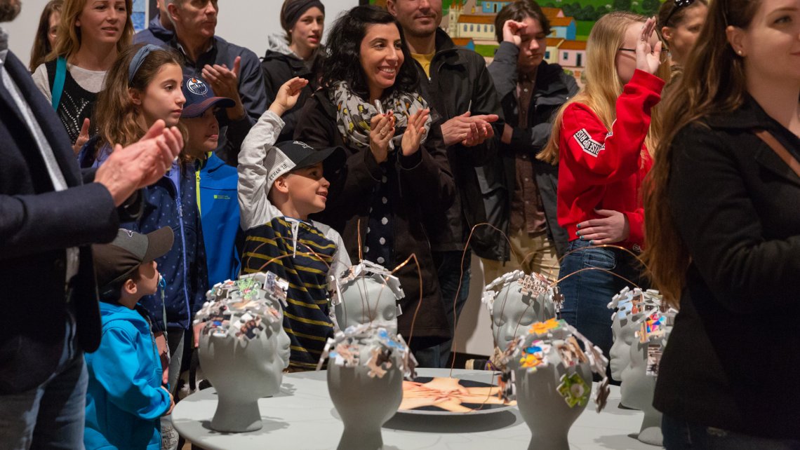 Group of people surrounding students' sculptural work in the youth exhibitoin Expressions
