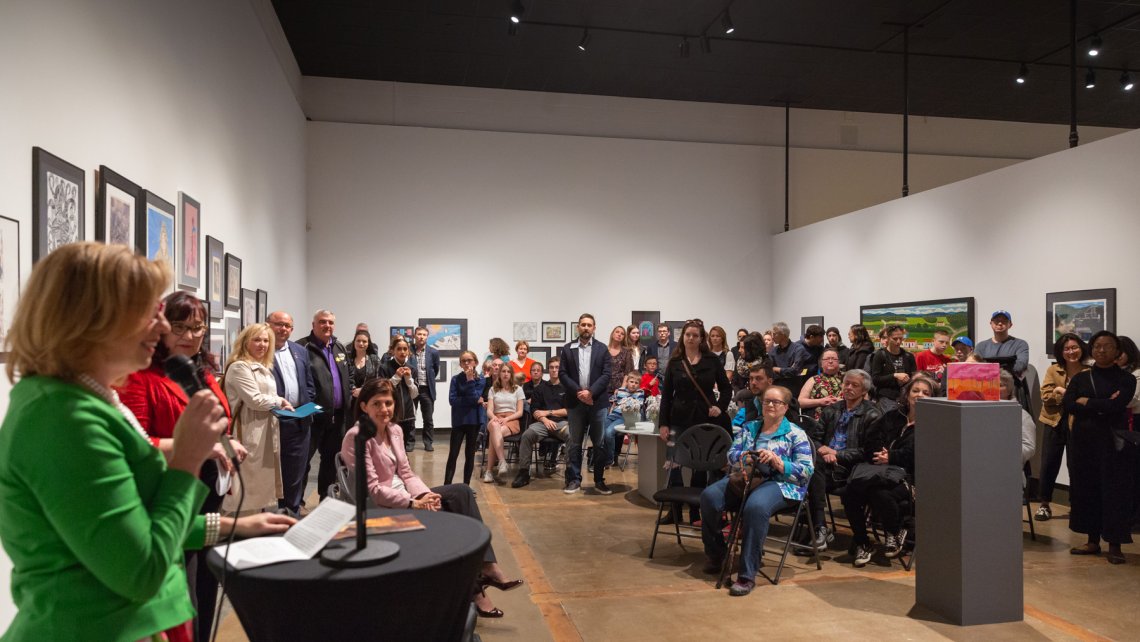 Crowd of people standing facing a speaker at the Expressions exhibition reception 