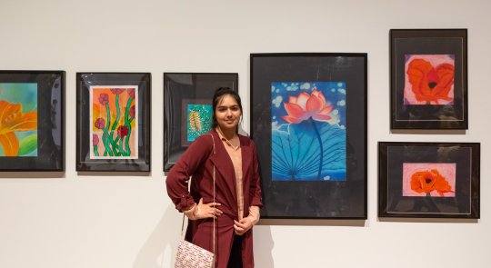 Young person standing in fromt of a white wall filled with student artwork