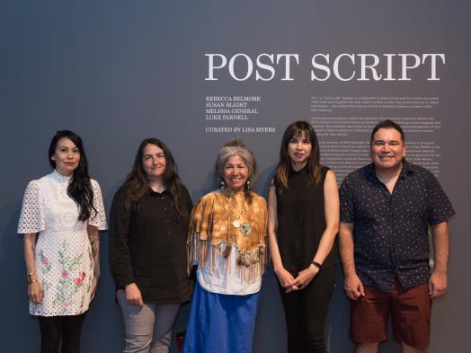 Susan Blight, Lisa Myers, Mary Anne Caibaiosai, Melissa General and Luke Parnell stand together in front of the title wall for Post Script