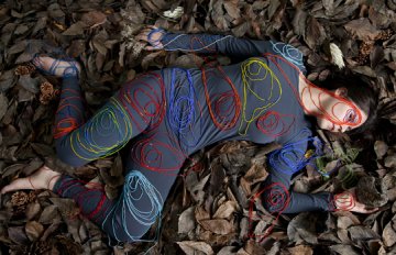 Photograph of a woman lying on the ground in a blue onesie with yarn shaped into circles and placed on her body